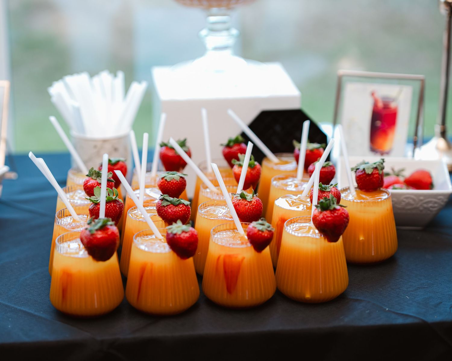 Orange pumpkin cocktails garnished with fresh strawberries and straws arranged on a dark slate surface.