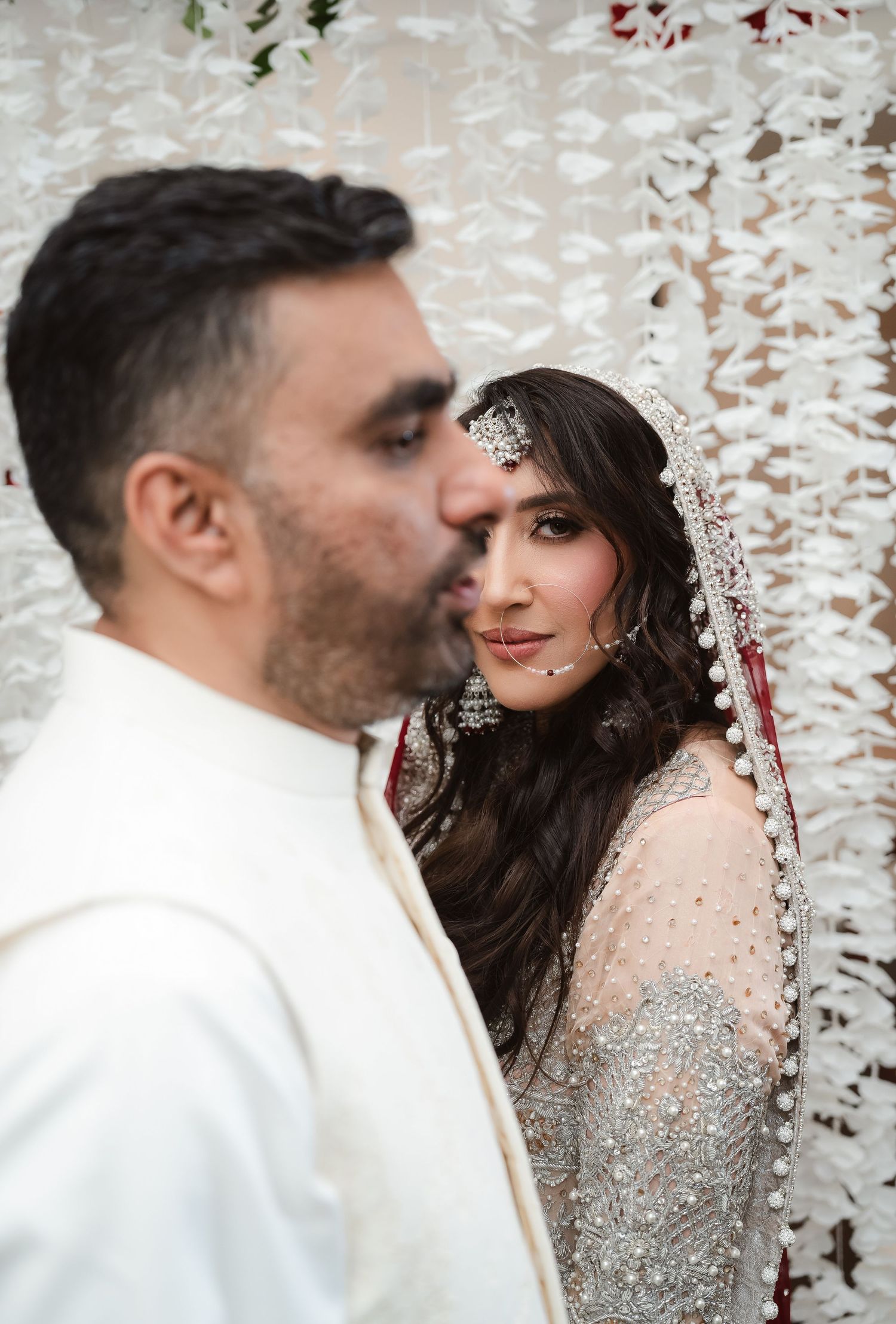 A romantic wedding couple embraces under falling confetti with the bride in a sparkly silver gown.