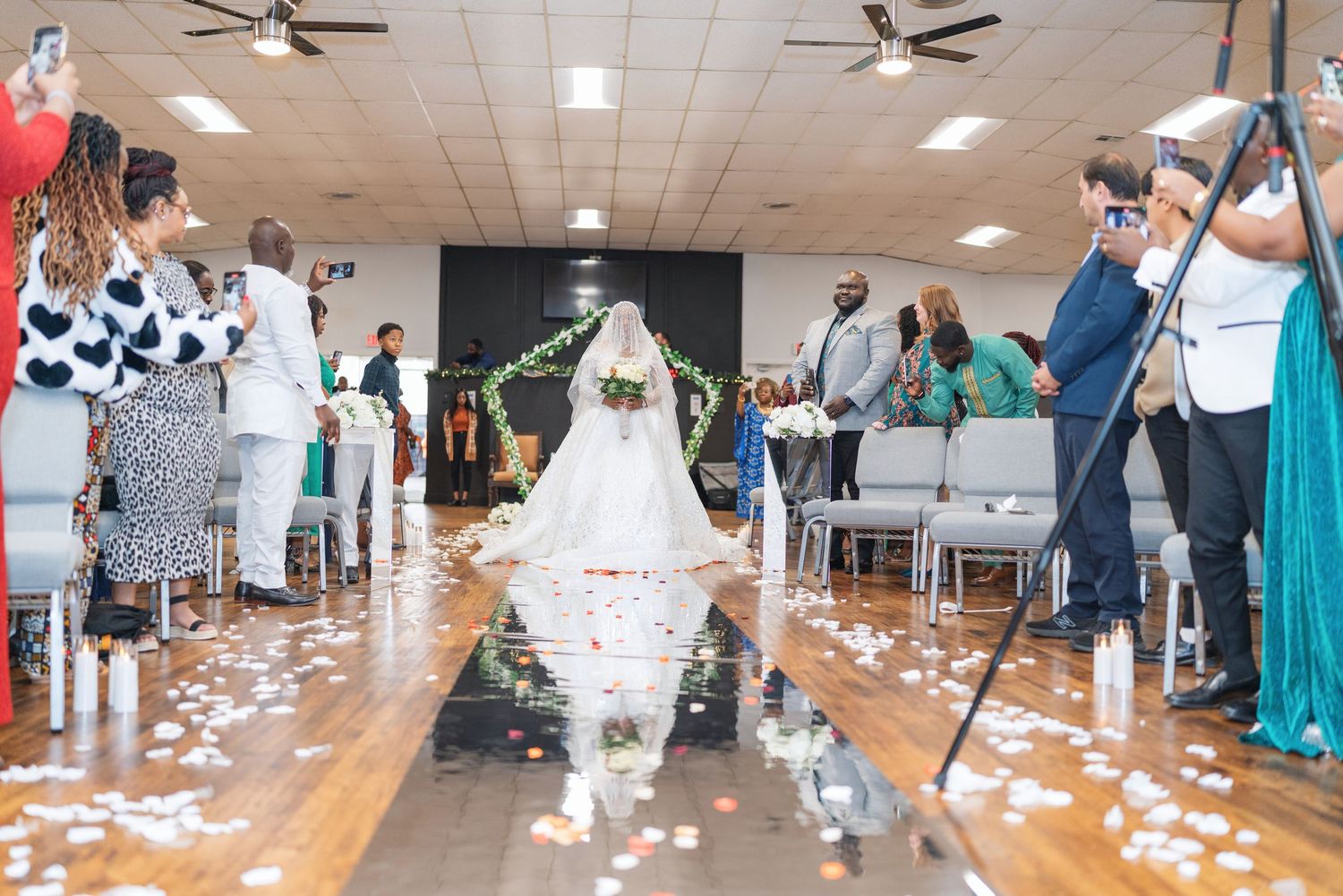 Wedding ceremony aisle covered in white petals with guests and photographers capturing the moment.