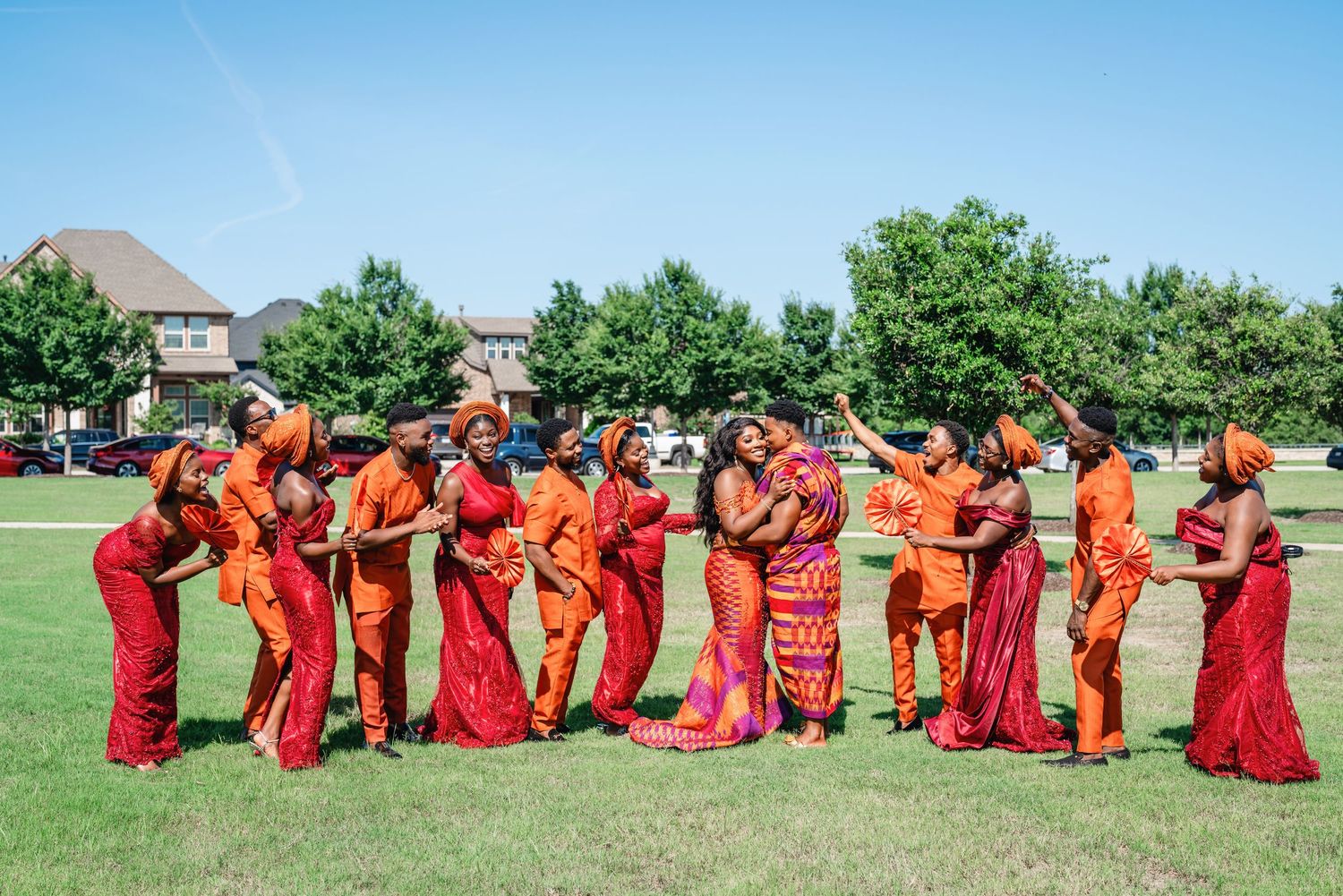 Wedding party members arranged in a fun domino-style pose on grass under blue sky.