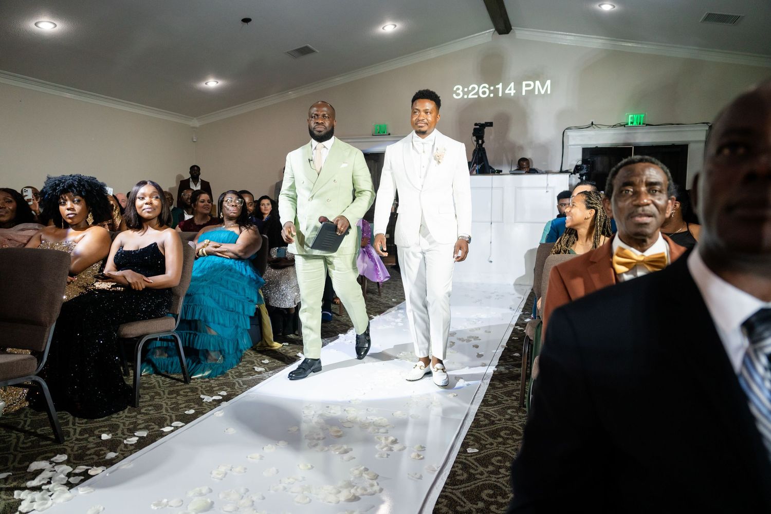 Two people walk down a runway at a formal event wearing all-white ensembles.