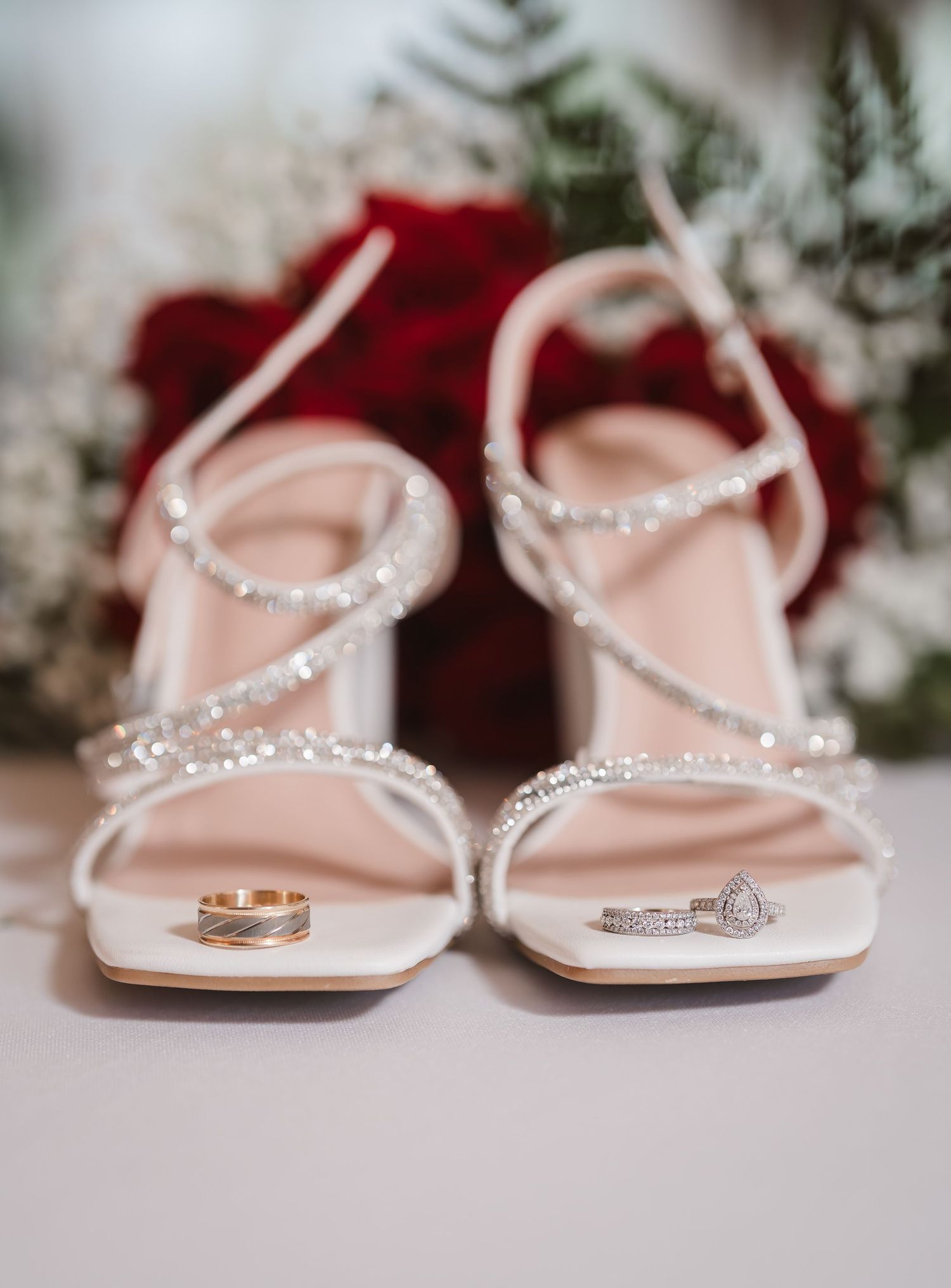 Elegant bridal sandals with crystal embellishments and wedding rings displayed on a light surface.