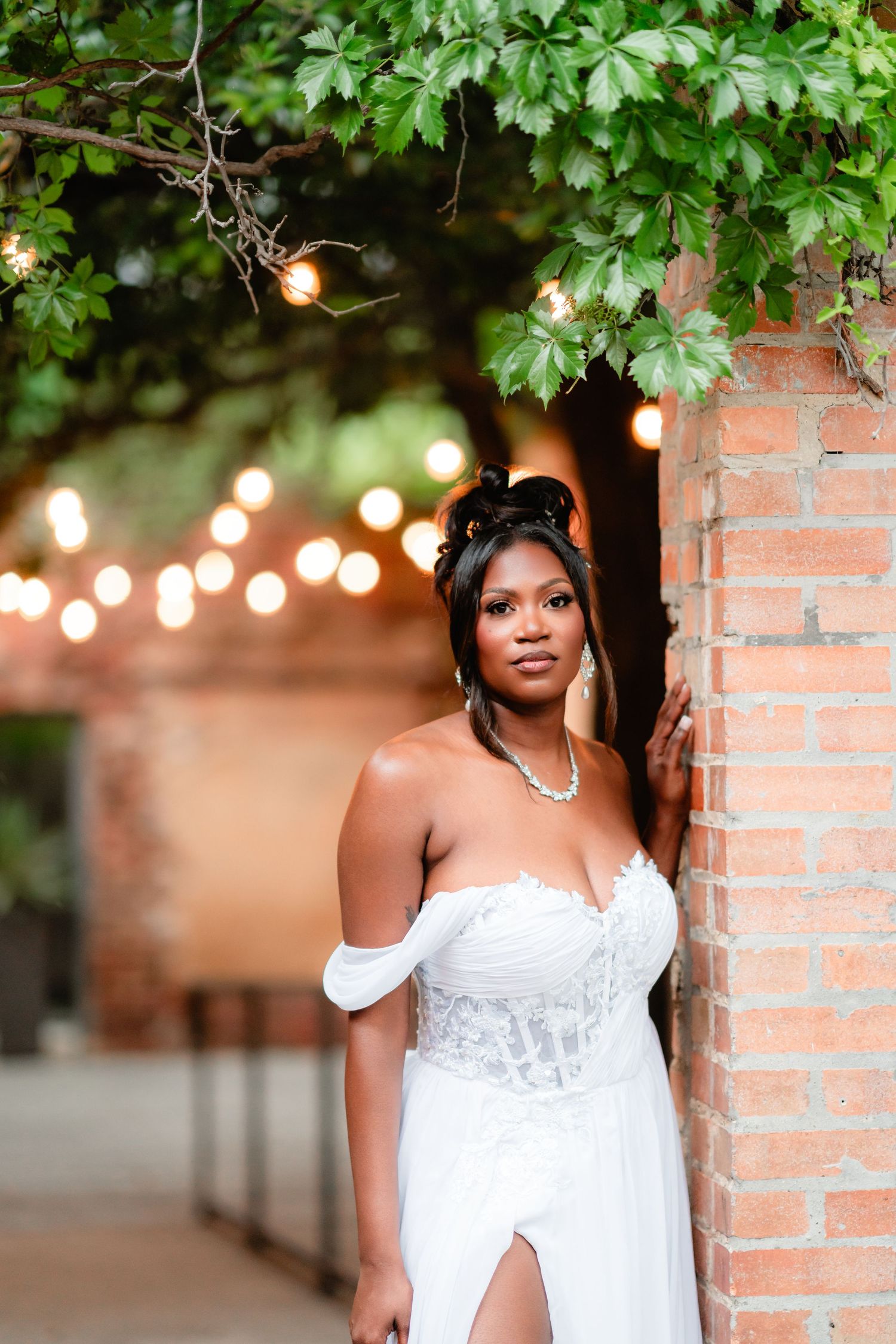 Beautiful bridal portrait with string lights and brick wall backdrop creating a romantic ambiance.