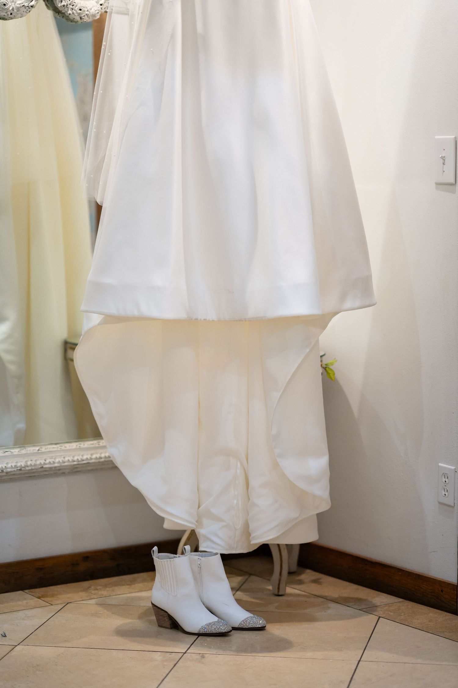 Close-up of white wedding dress hem and boots on tiled floor showing elegant bridal details.