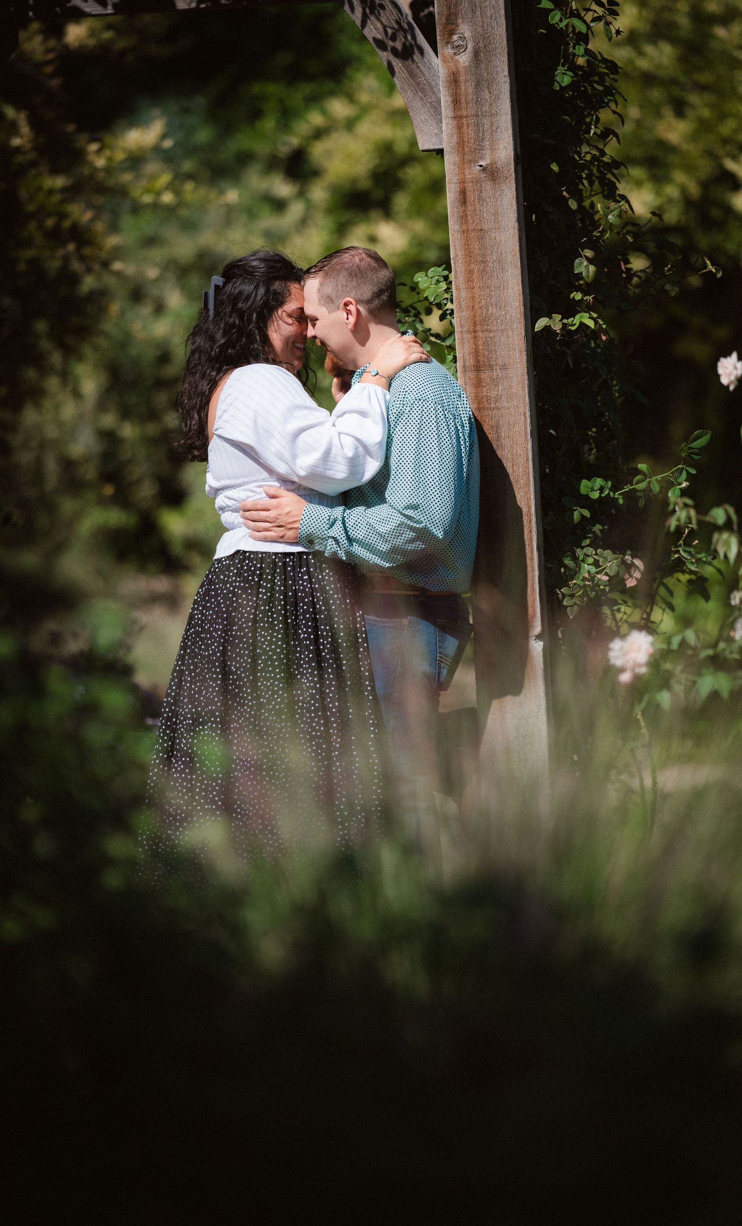 An intimate moment shared between a couple in a rustic garden setting framed by wooden posts.