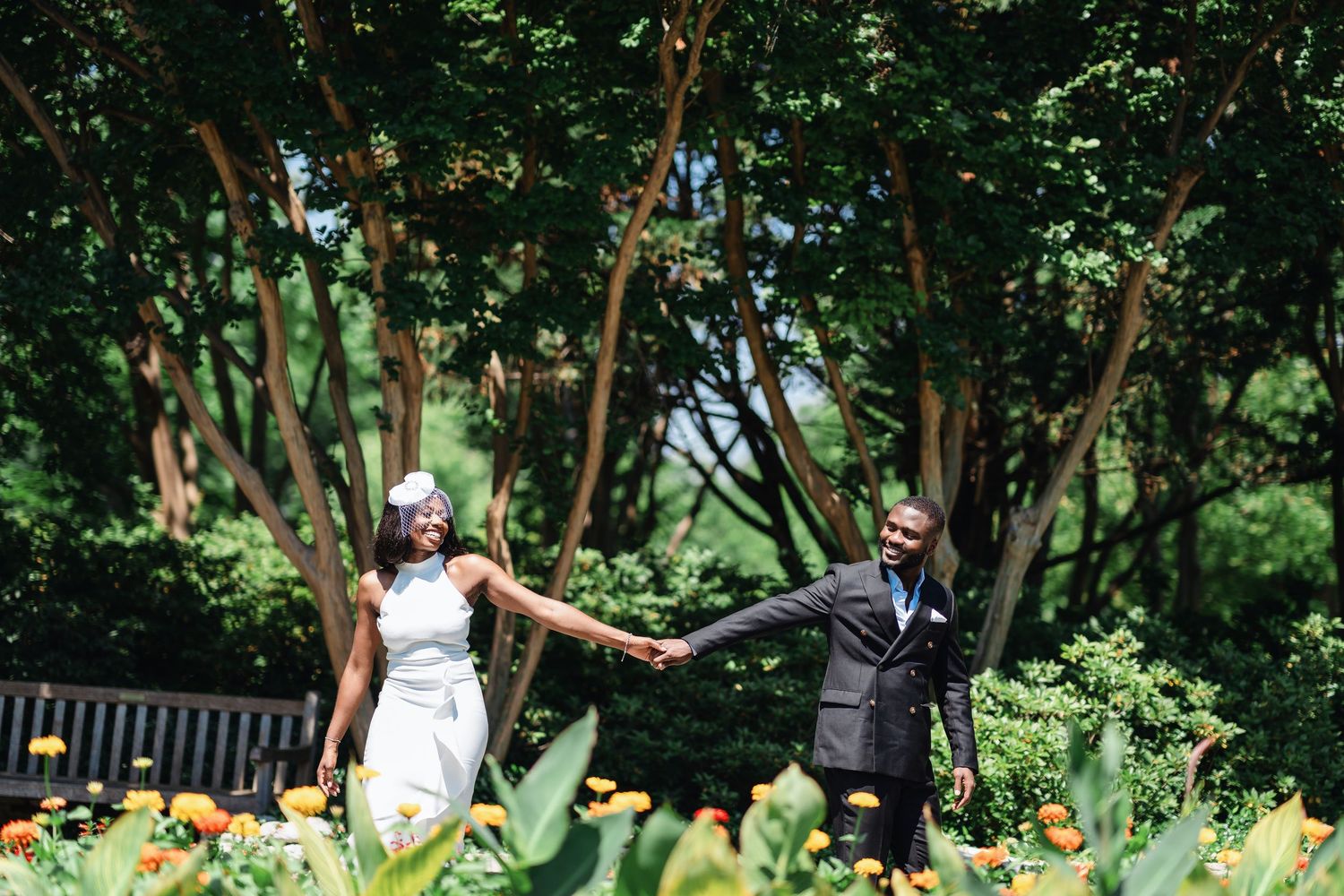 A couple shares a playful moment in a beautiful outdoor garden with blooming flowers and tall plants.