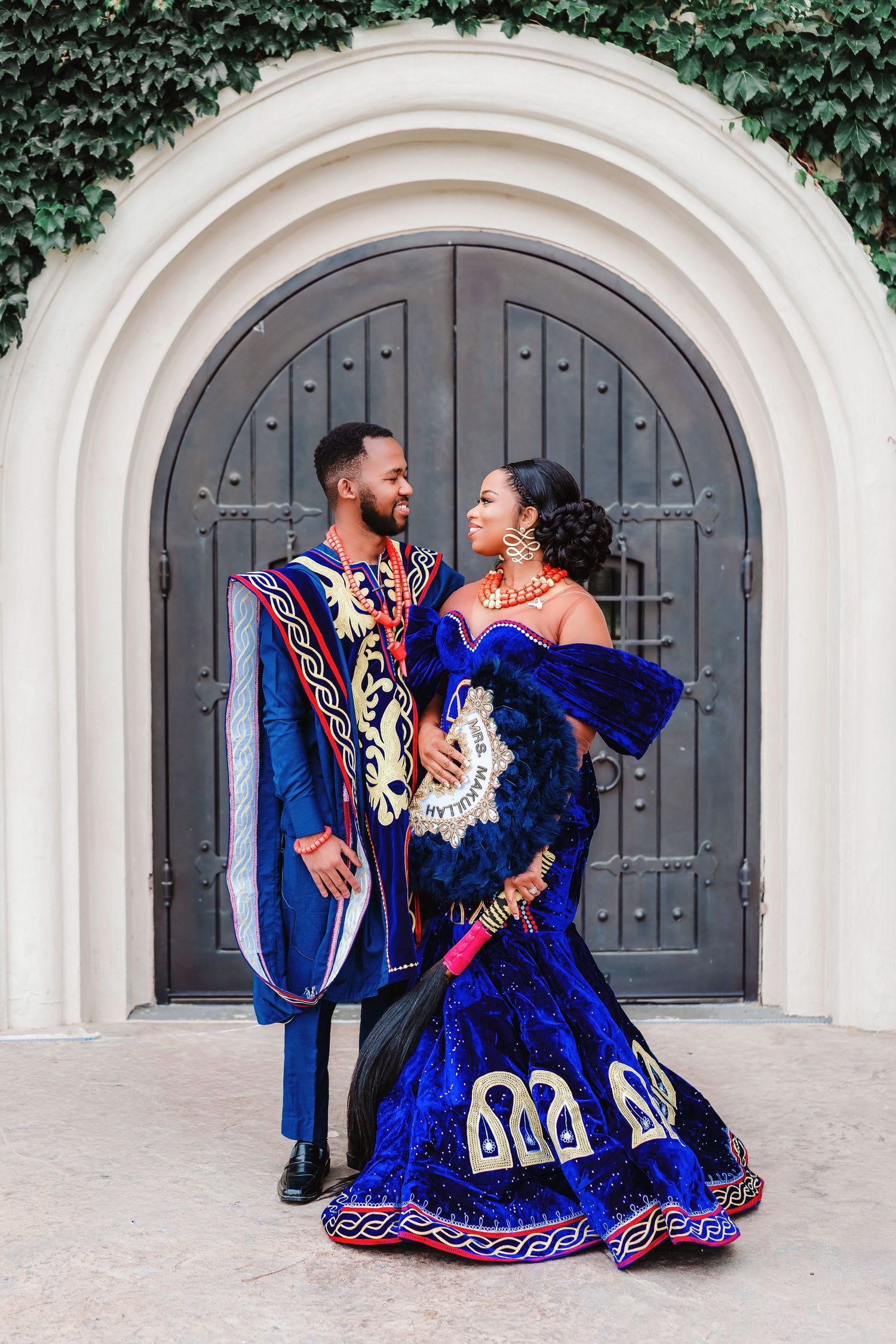 A couple in elegant blue formal wear dances and poses romantically against ornate doorways.