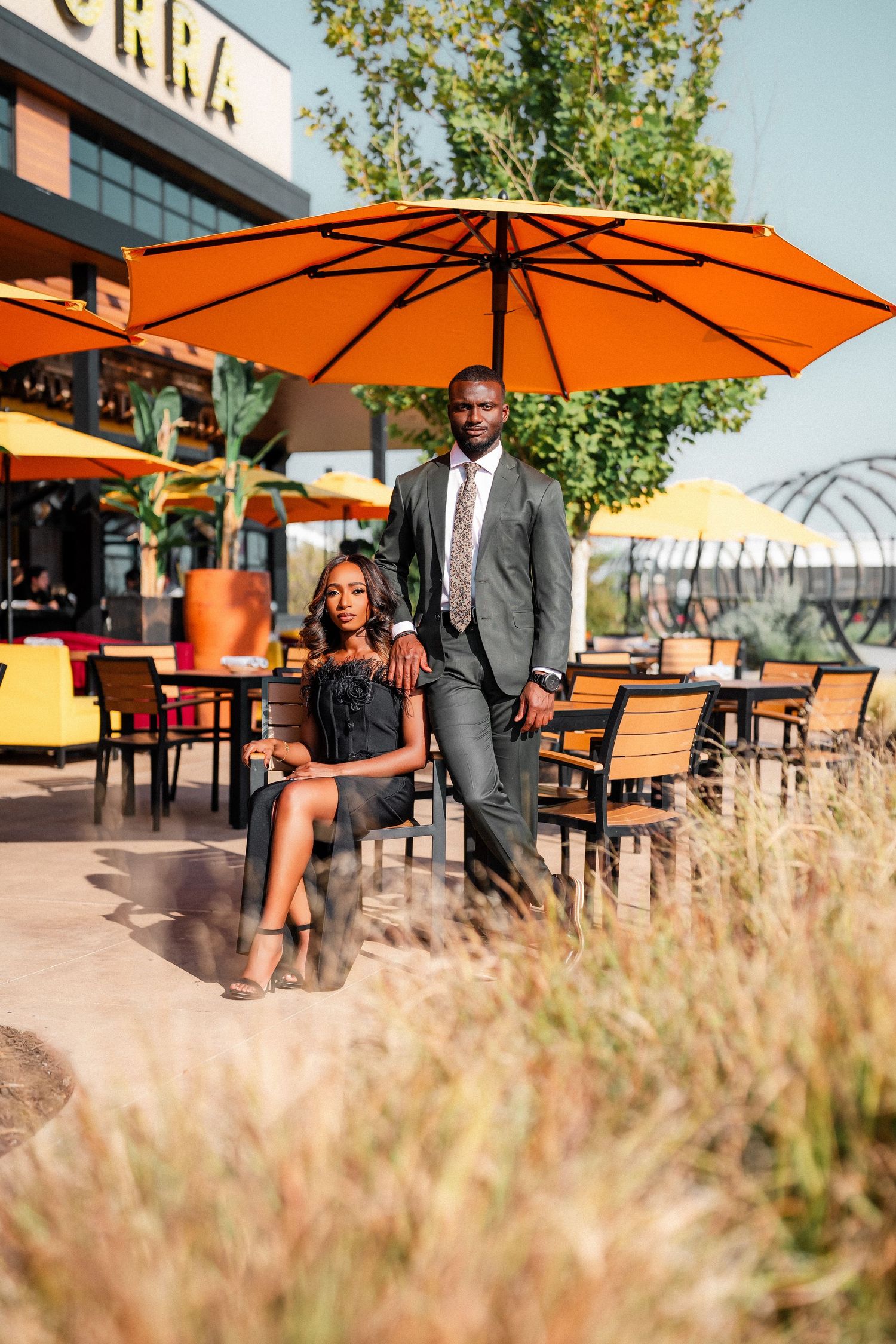 Elegant couple posing at an outdoor restaurant patio with orange umbrellas.