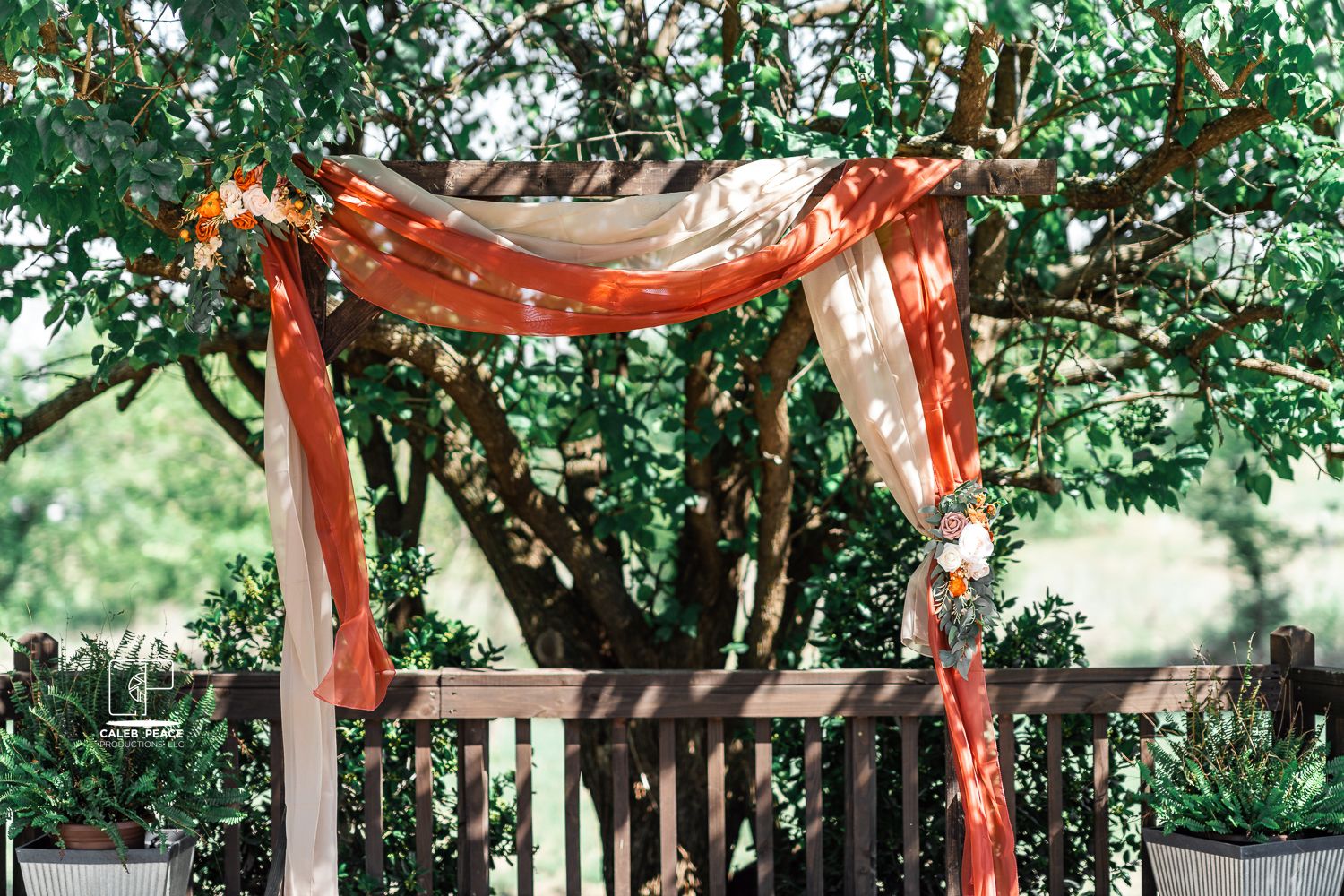 Outdoor wedding ceremony setup with orange and white draped fabric canopy among green trees.