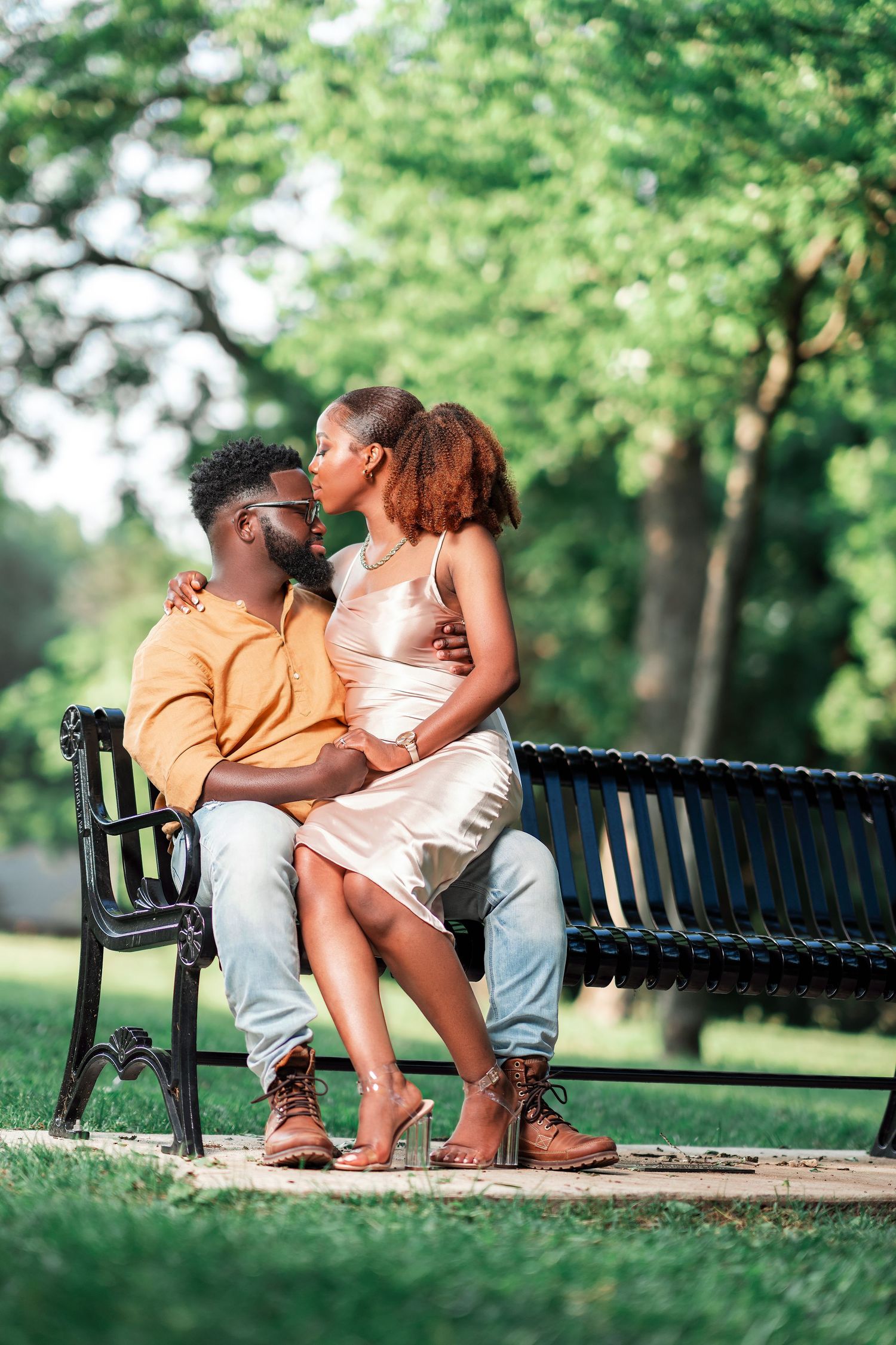 A tender moment shared between two people sitting close together on a park bench surrounded by lush green trees.