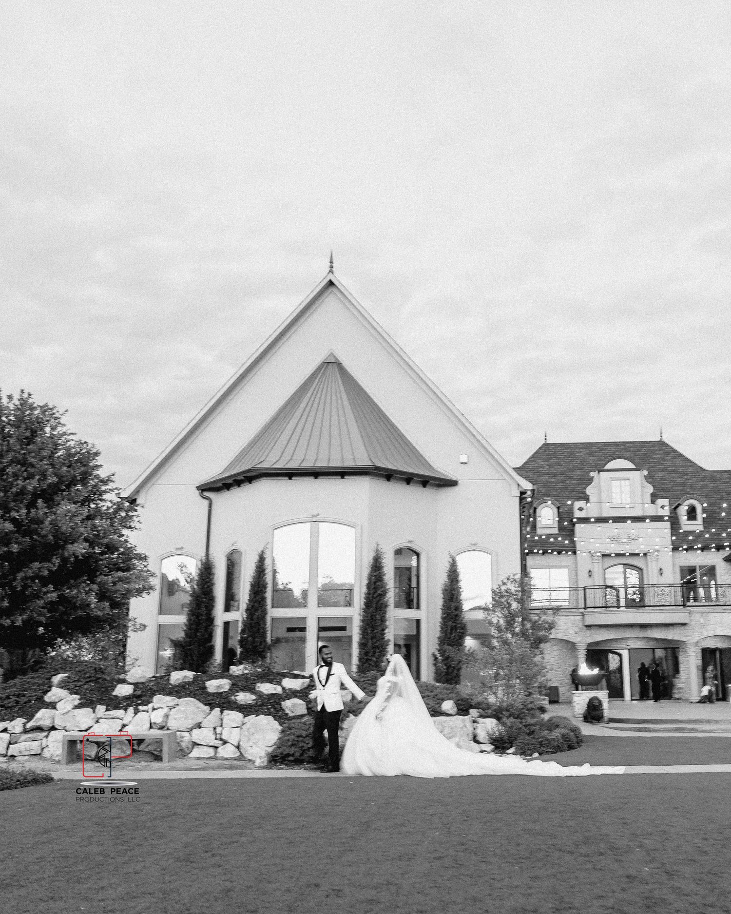 A series of white wedding venue buildings with peaked roofs and architectural details line a grassy lawn under cloudy skies.