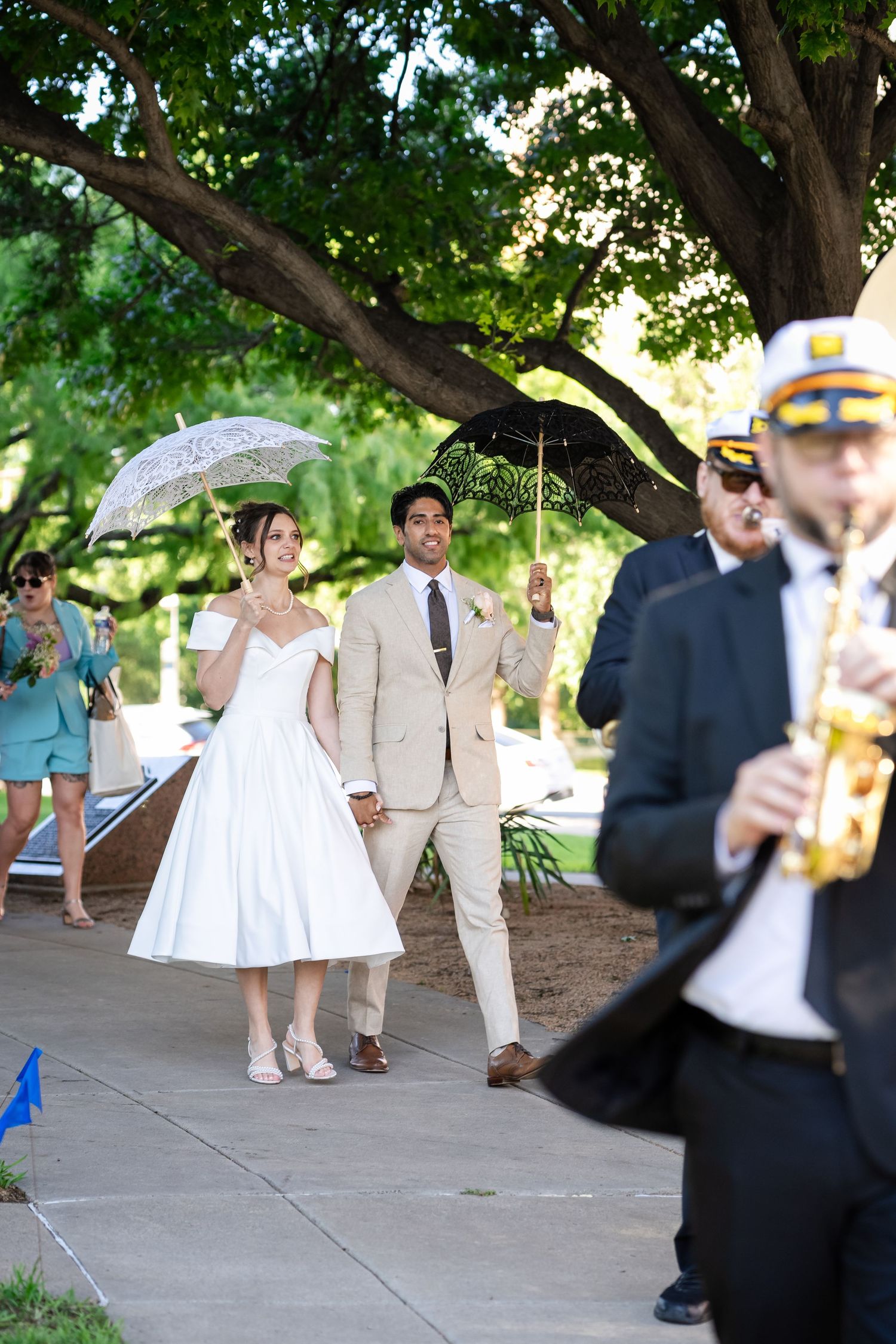 Wedding party members walk and celebrate along a tree-lined path during an outdoor celebration.