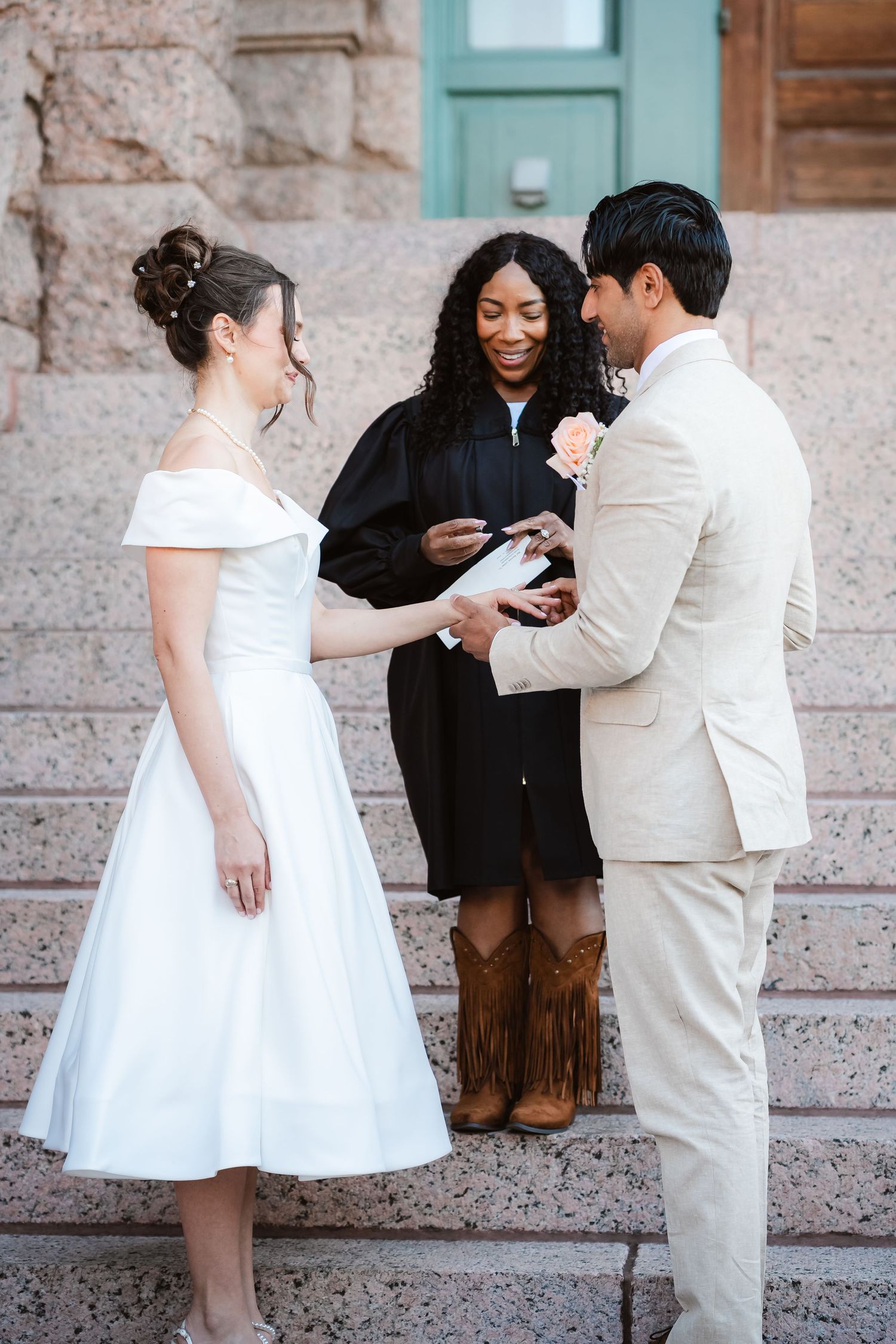 Wedding ceremony participants gather on stone steps outside a building with turquoise accents.
