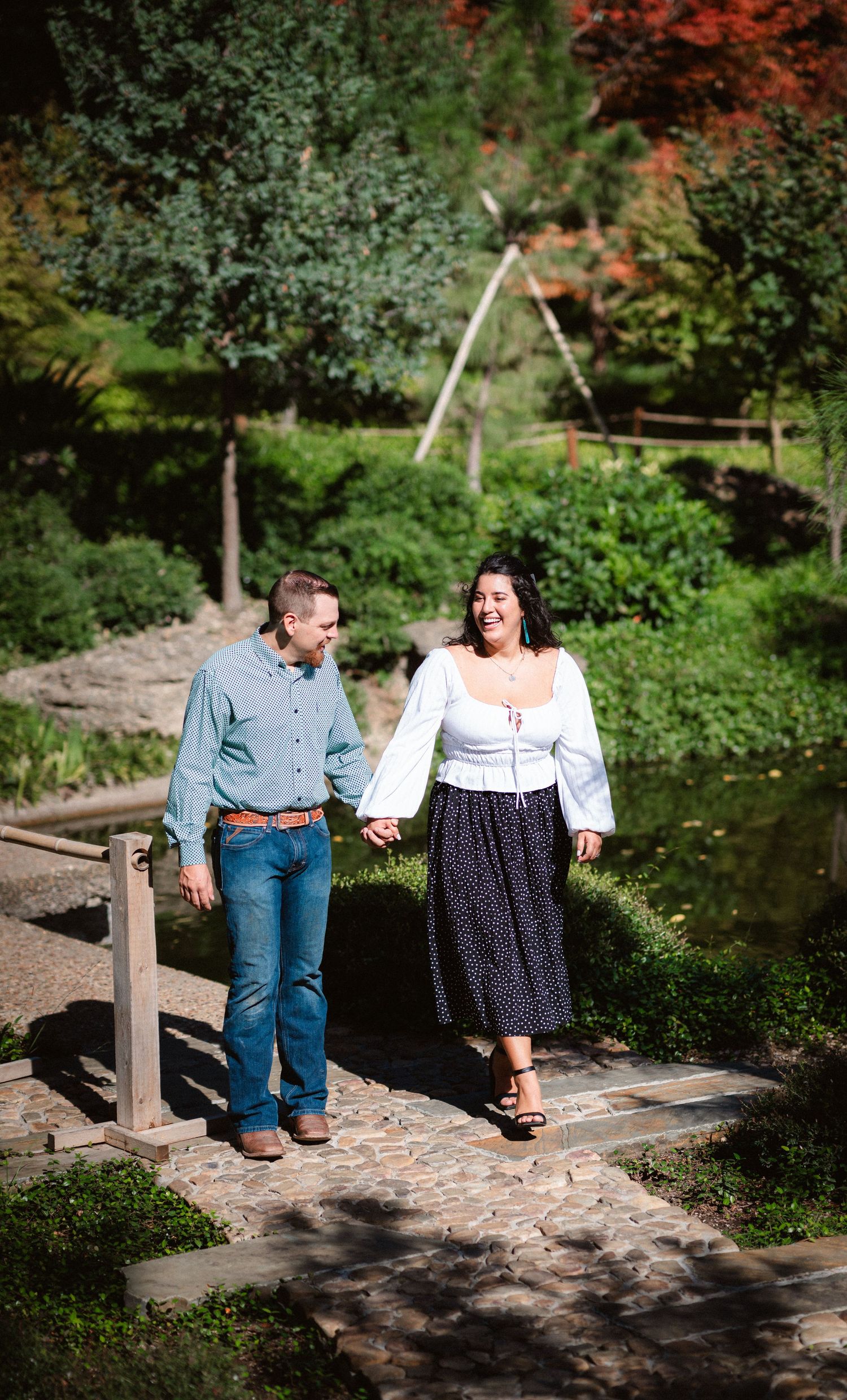 Couple sits together on a wooden bridge in a lush garden setting during a romantic photoshoot.