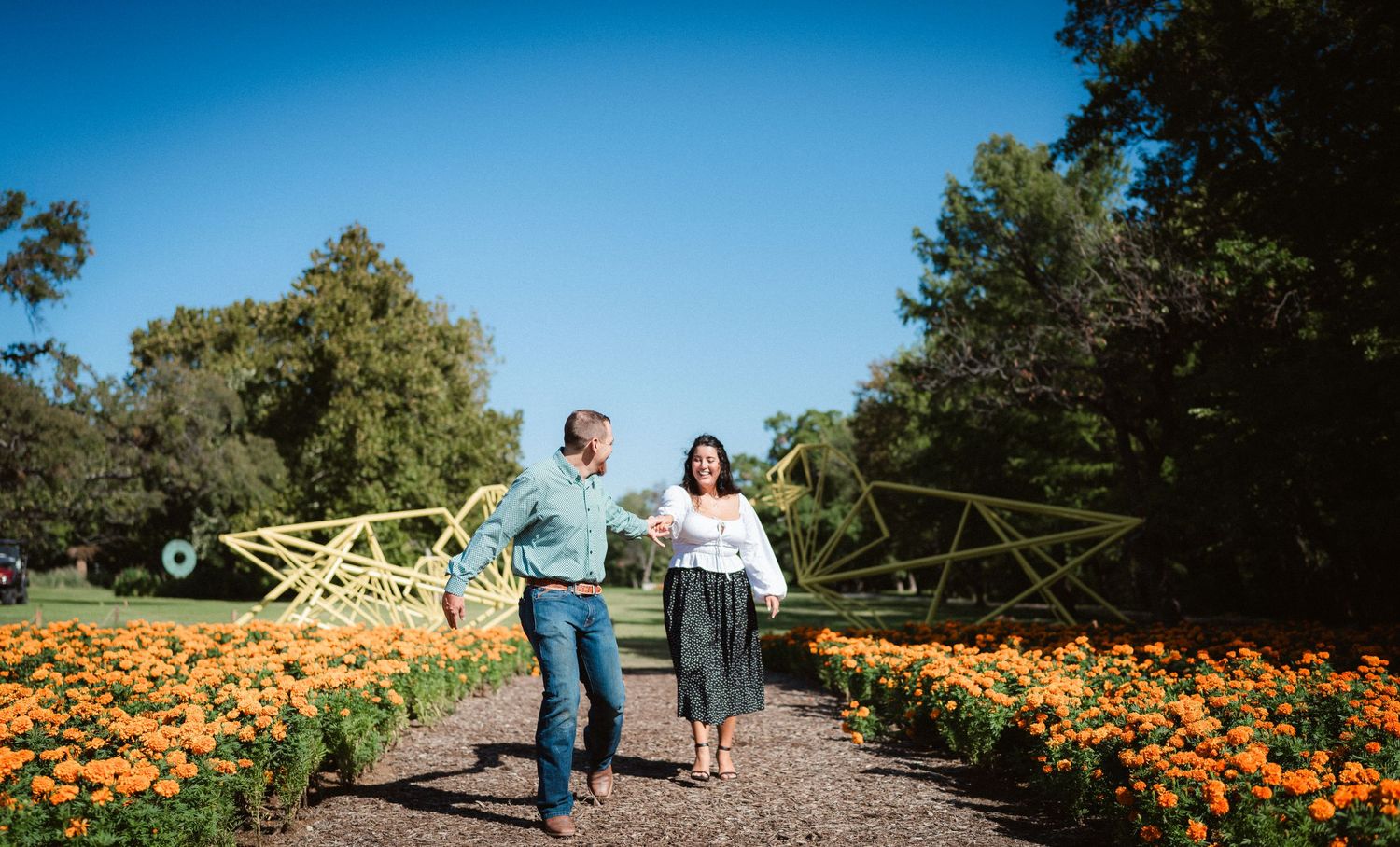 A romantic couple strolls through a vibrant orange poppy field on a sunny day.