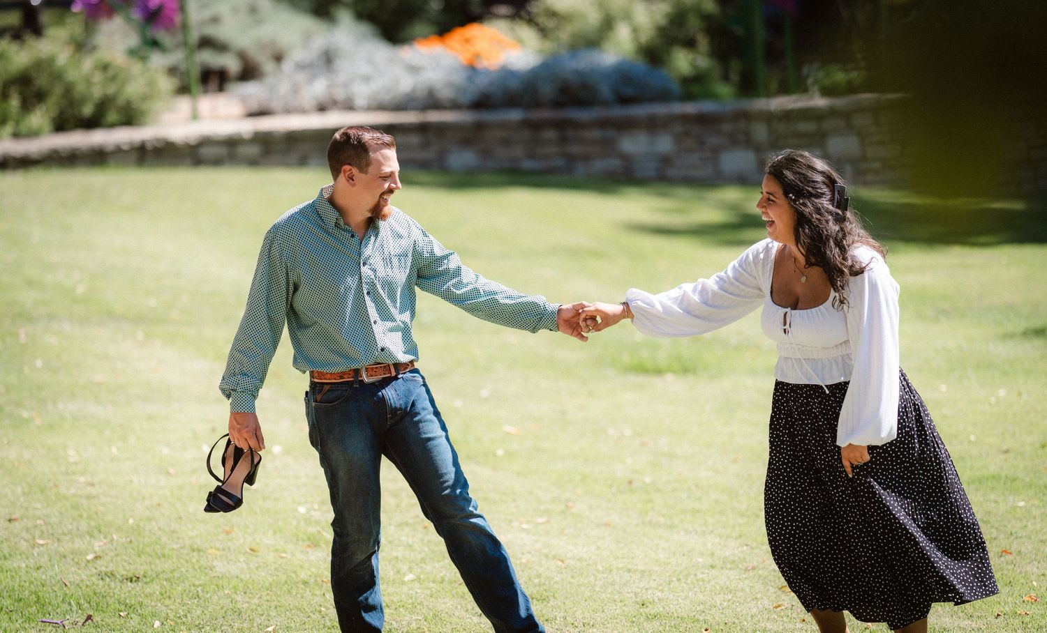 Couple interacting playfully in a sunny garden setting with green grass and trees.