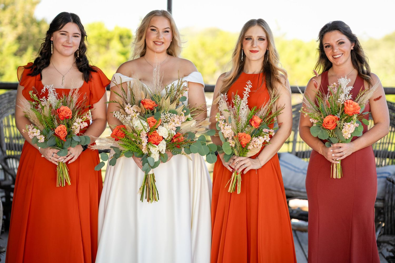 Bridal party with bridesmaids in coral dresses holding matching floral bouquets.