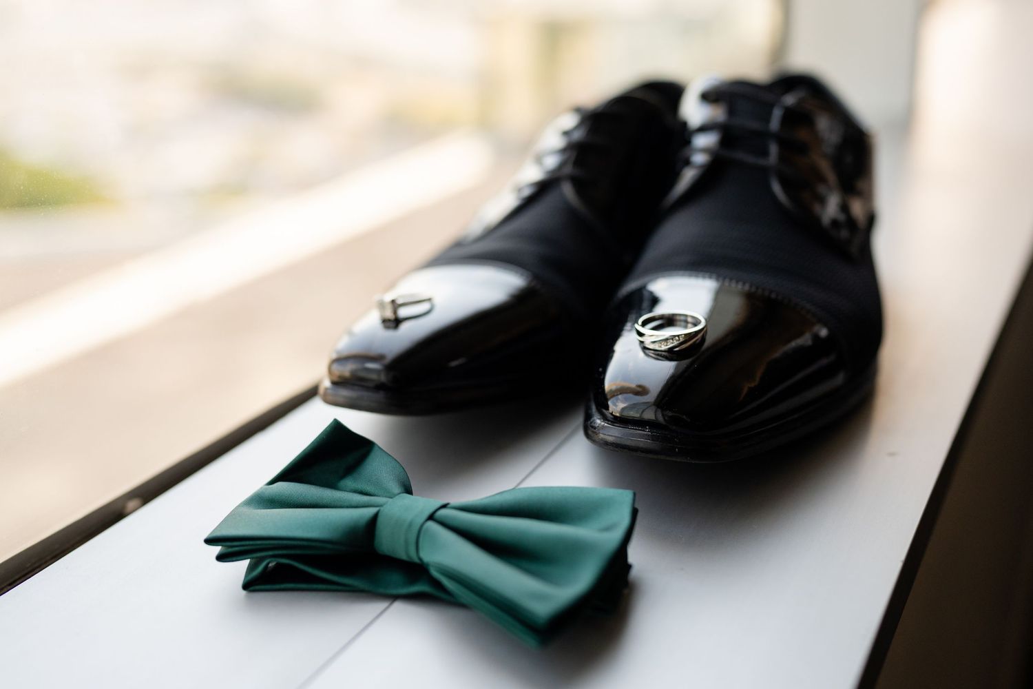 Close-up of formal black dress shoes and emerald green bow tie as wedding accessories.