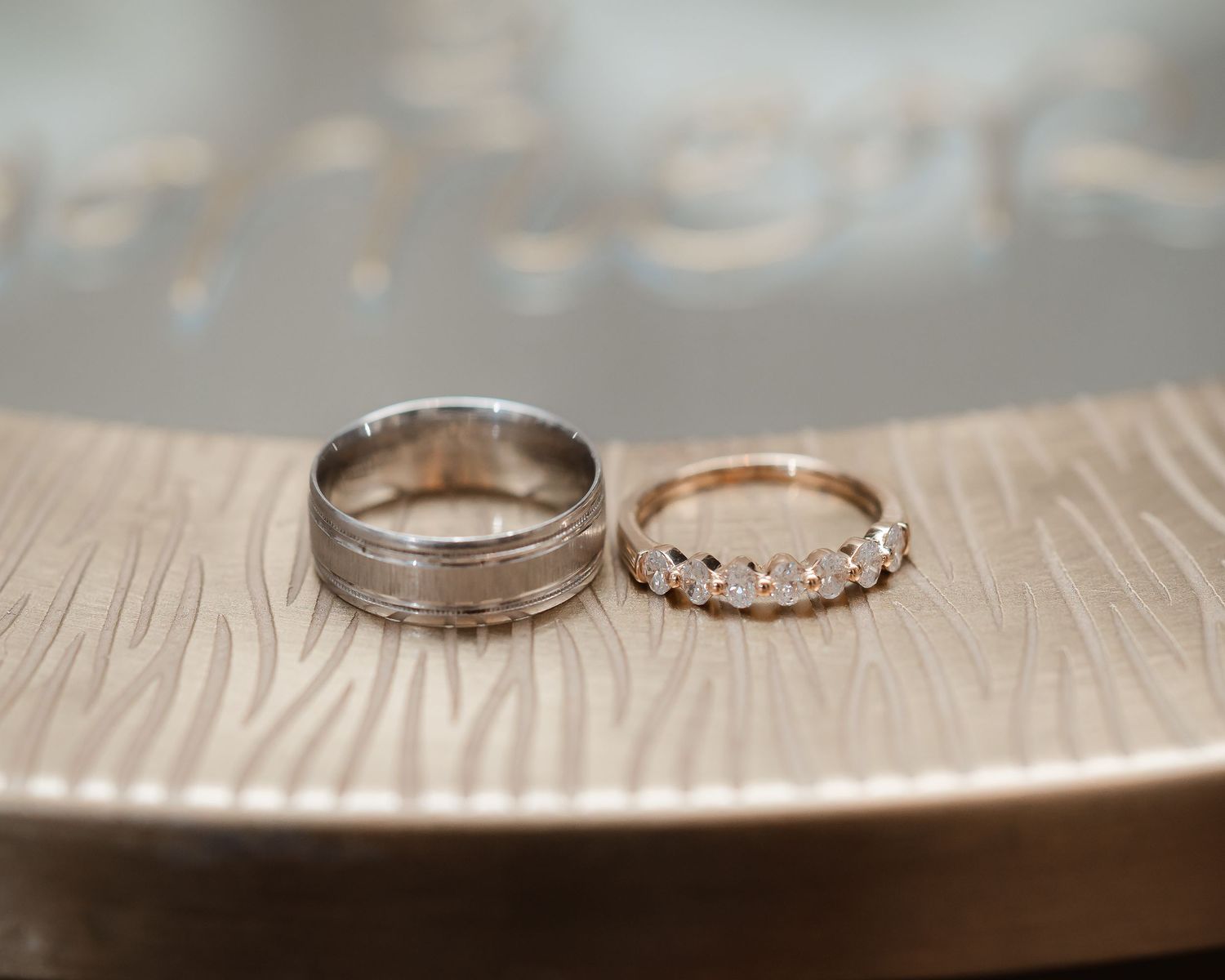 Wedding rings sit on a textured surface with soft bokeh lighting in the background.