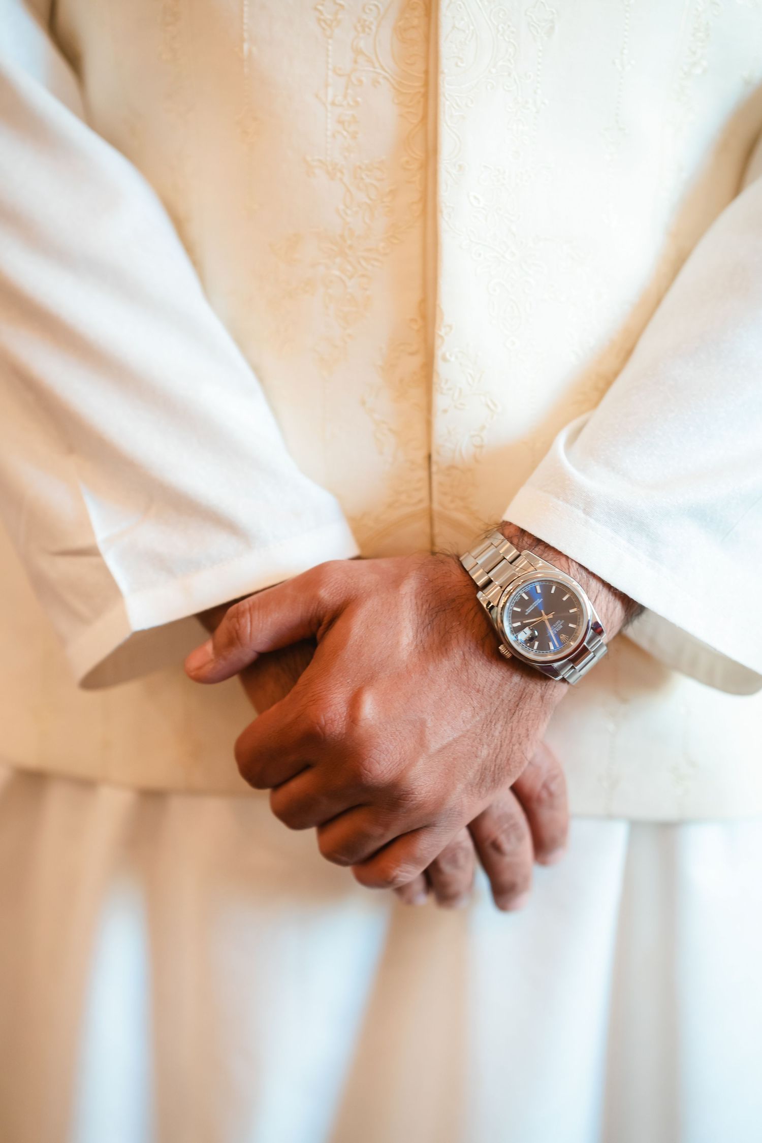 Person wearing white formal attire adjusts sleeves while displaying silver wristwatch.