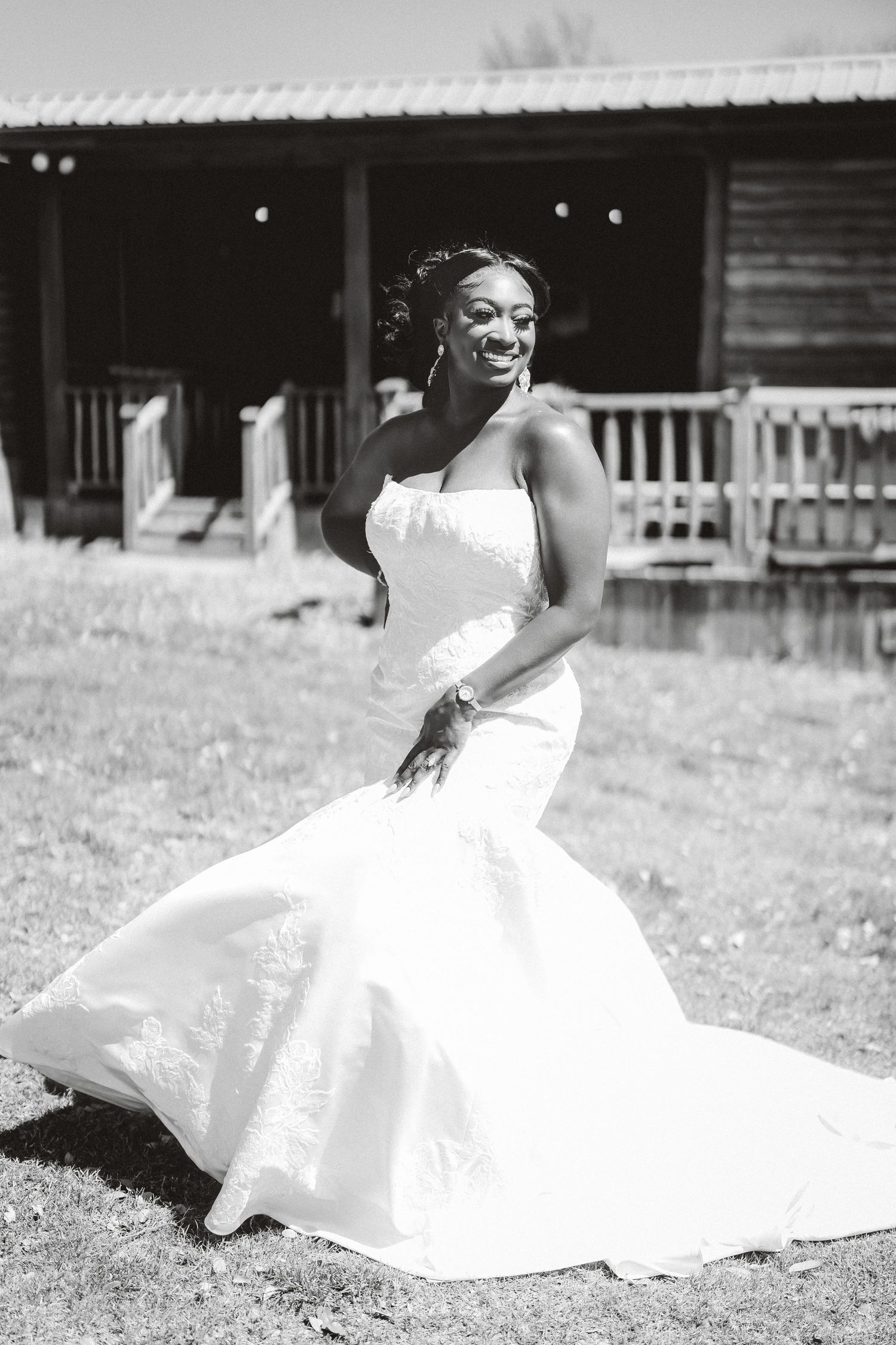 A bride in a flowing white wedding dress poses gracefully on a grassy lawn.