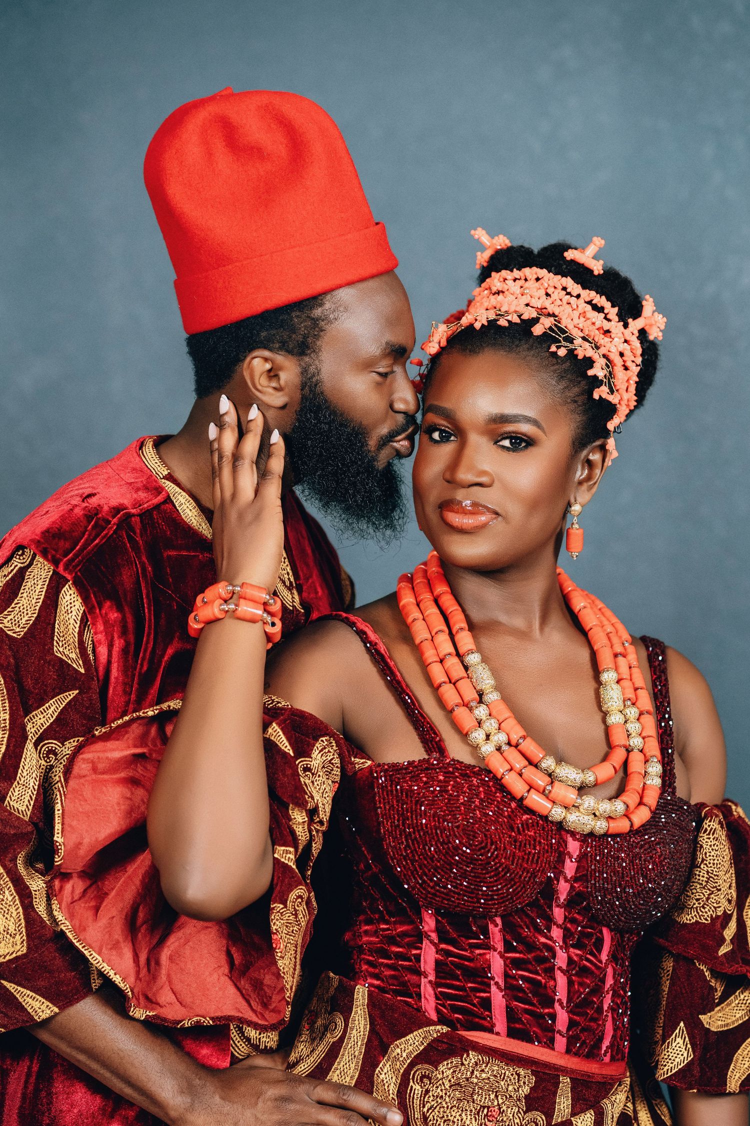 A couple in traditional Nigerian wedding attire with red and gold colors share intimate moments in a photo series.