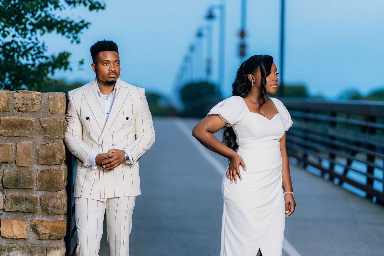 Couple in matching white outfits posing together on a waterfront walkway at dusk.