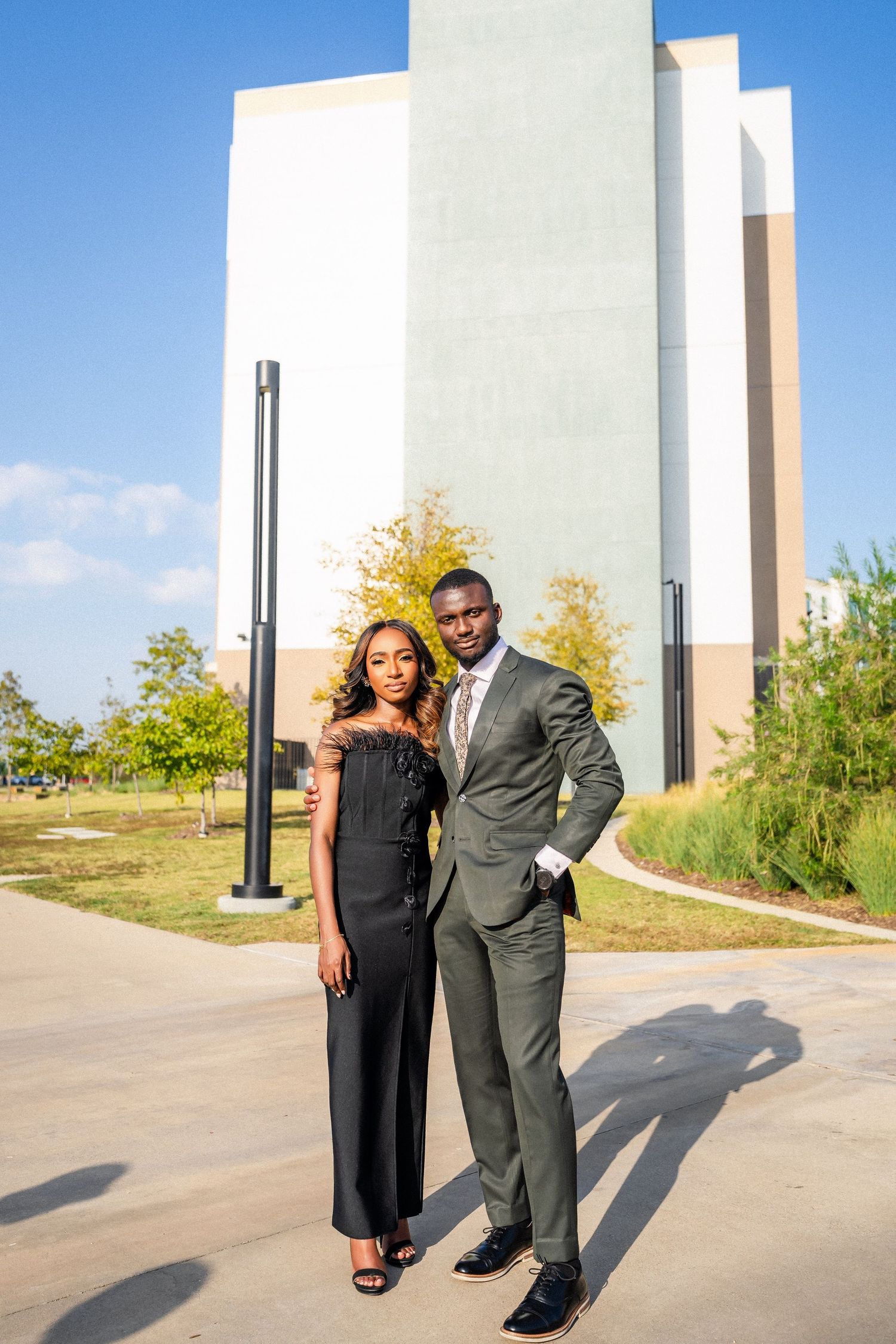 Elegant couple in formal wear posing together against modern architecture.