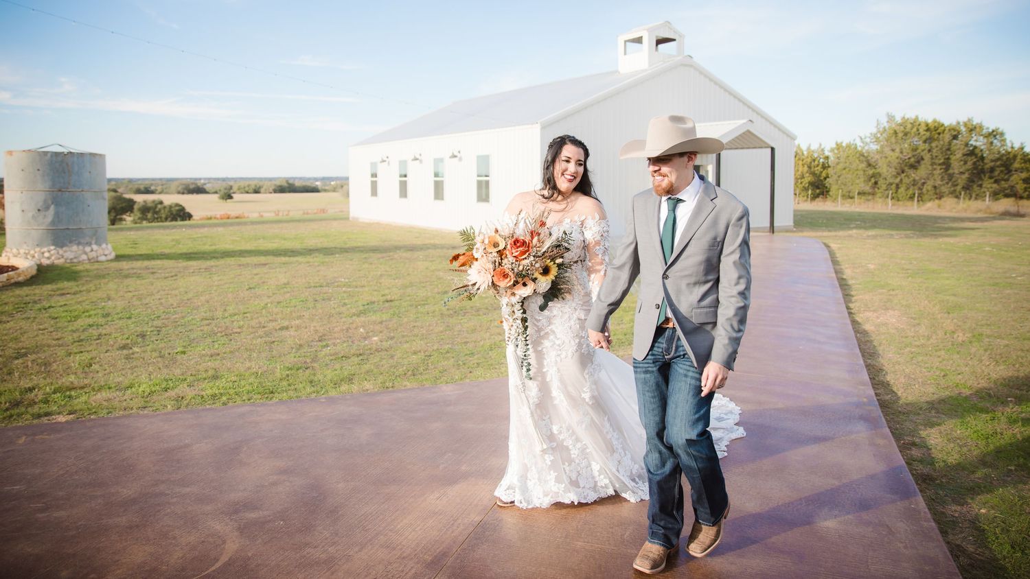A couple walks along a pathway outside a white barn-style building during sunset.