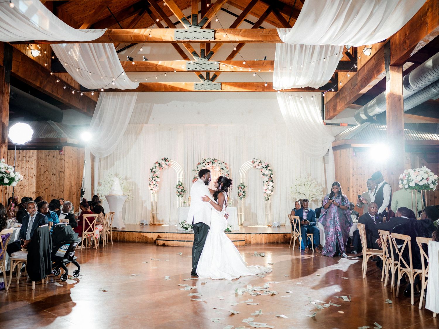 First dance of newlyweds under draped fabric and floral arch in rustic reception venue.