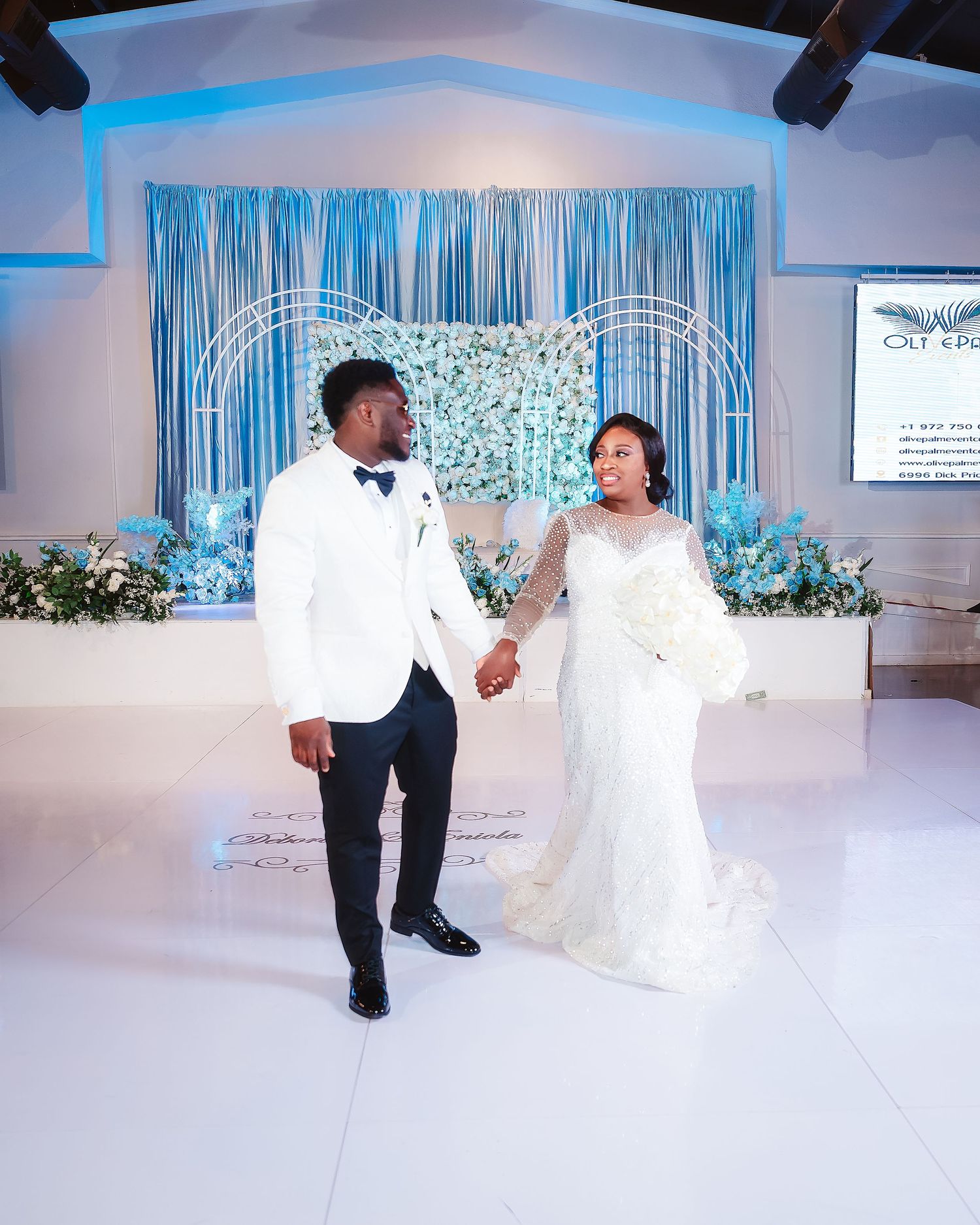 Wedding couple performs fun dance moves during their first dance at a reception with blue lighting and floral decor.