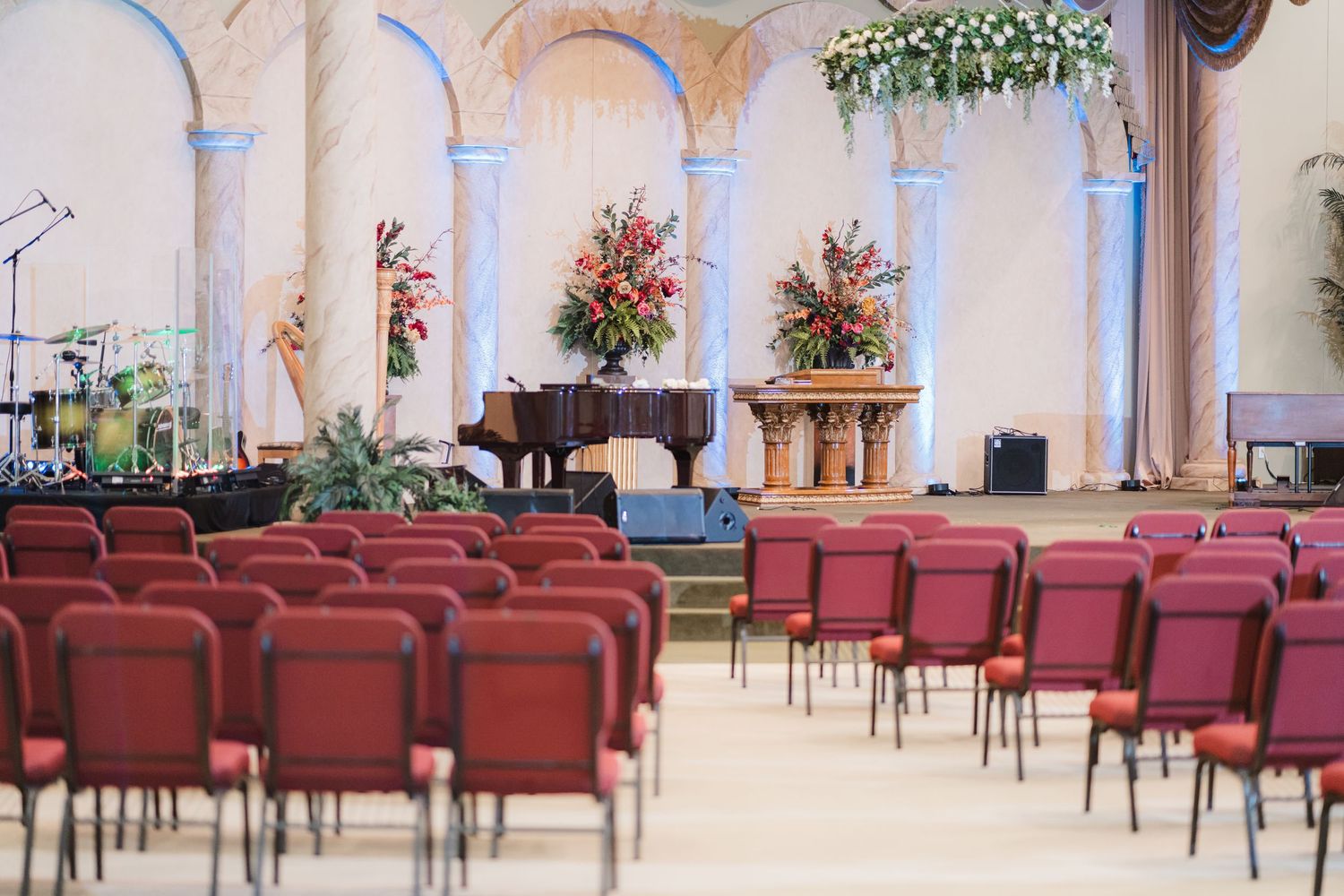 Church sanctuary decorated with floral arrangements and red chairs for wedding ceremony.