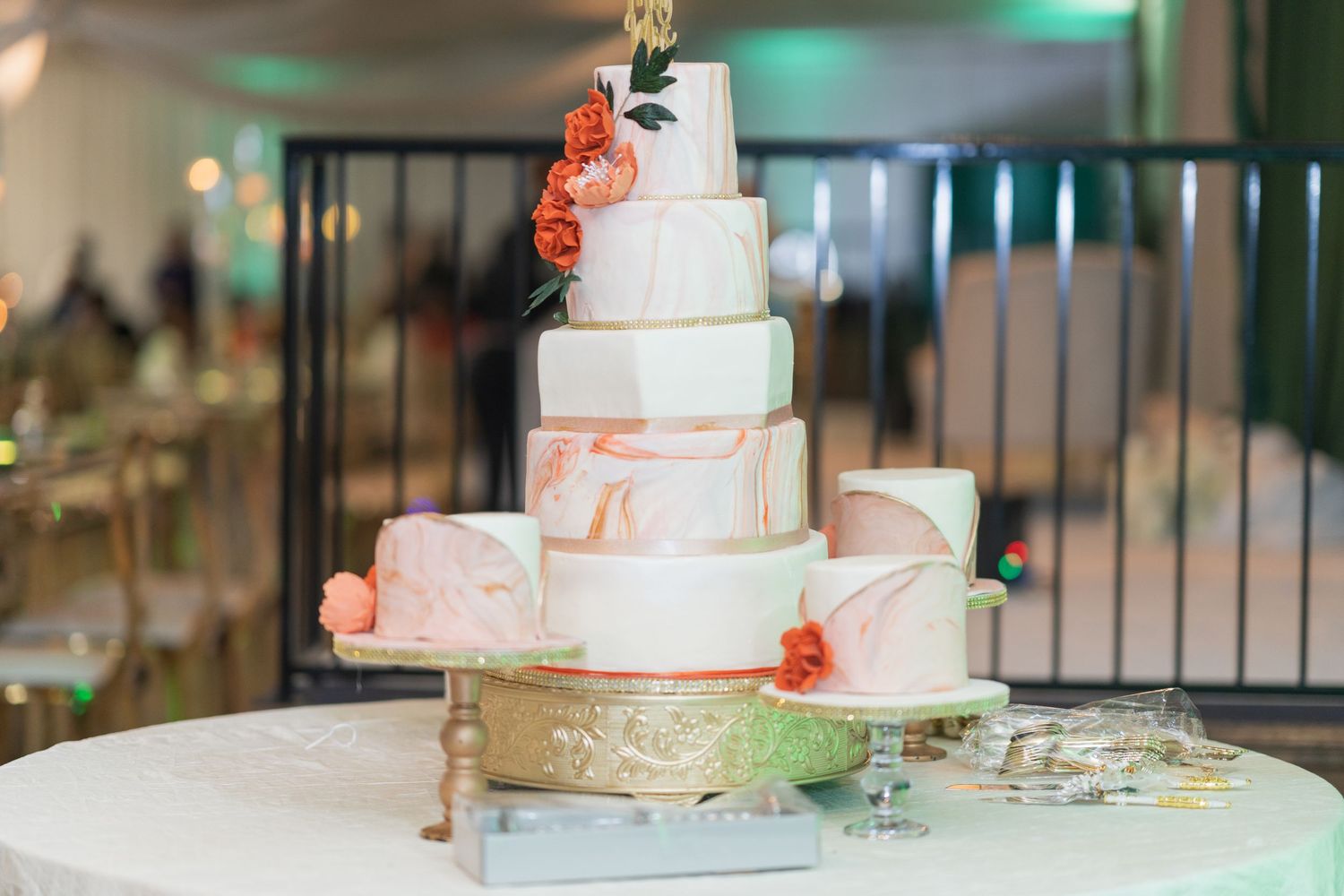 Elegant multi-tiered white wedding cake with coral floral accents displayed at reception venue.