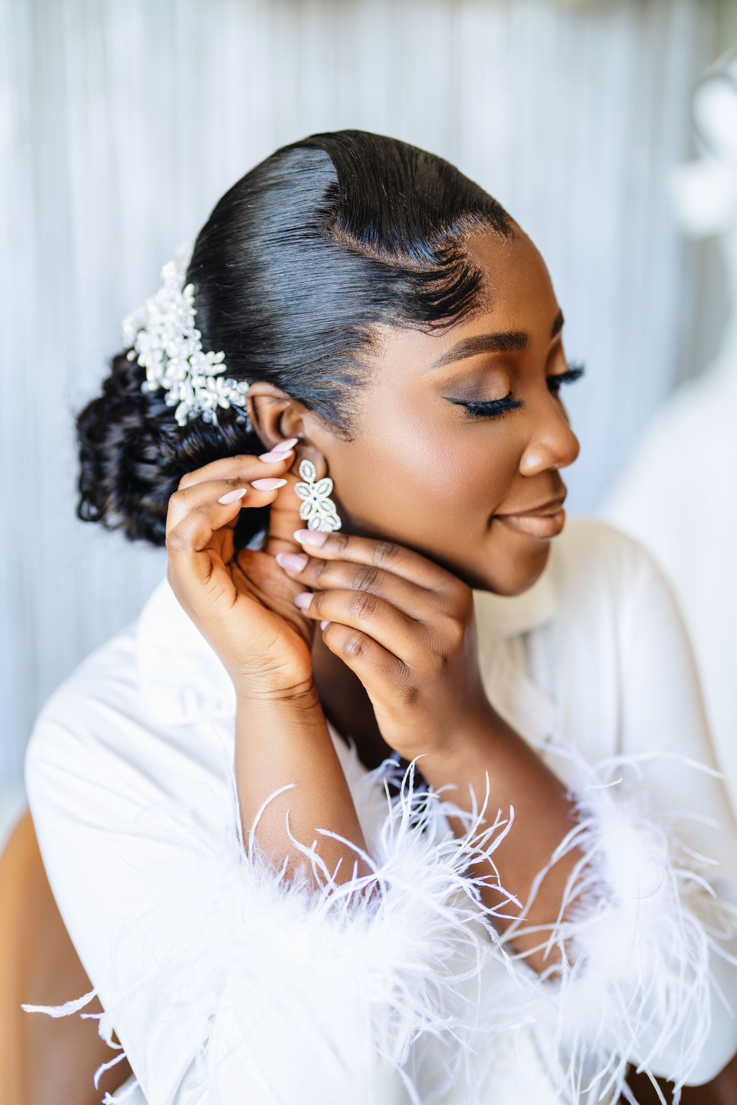 Elegant bridal portrait showing delicate feather details and sparkling hair accessories against a light background.