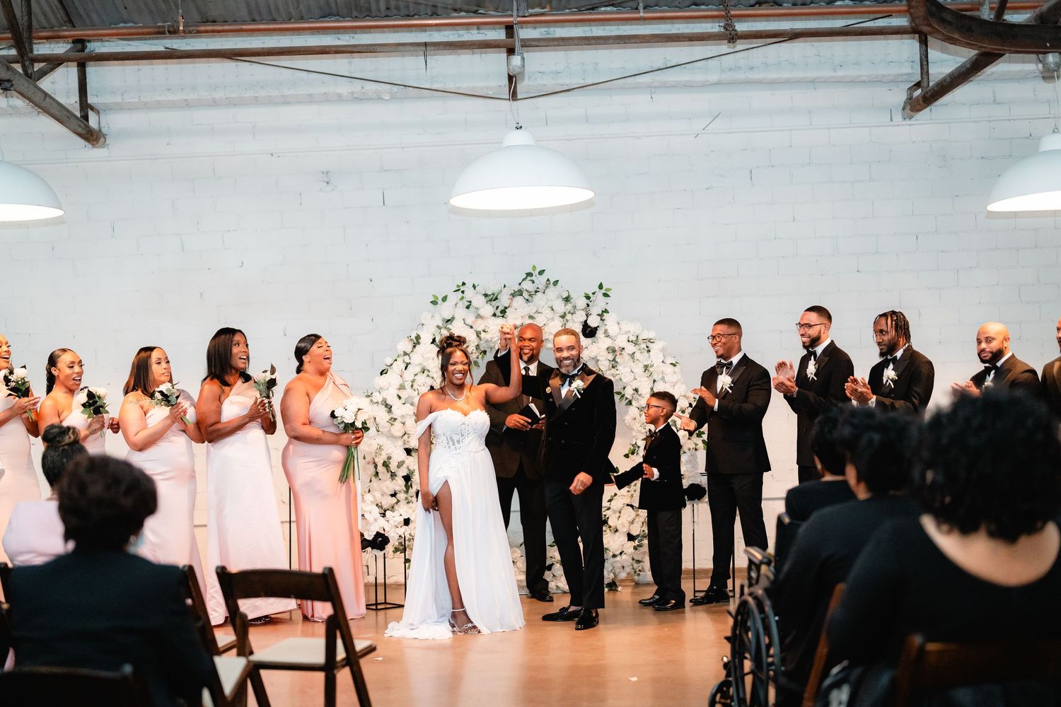Wedding ceremony in progress inside an industrial venue with guests seated on wooden chairs.