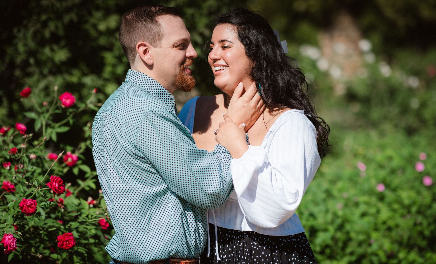 A romantic couple shares tender moments together in a garden with blooming red roses.