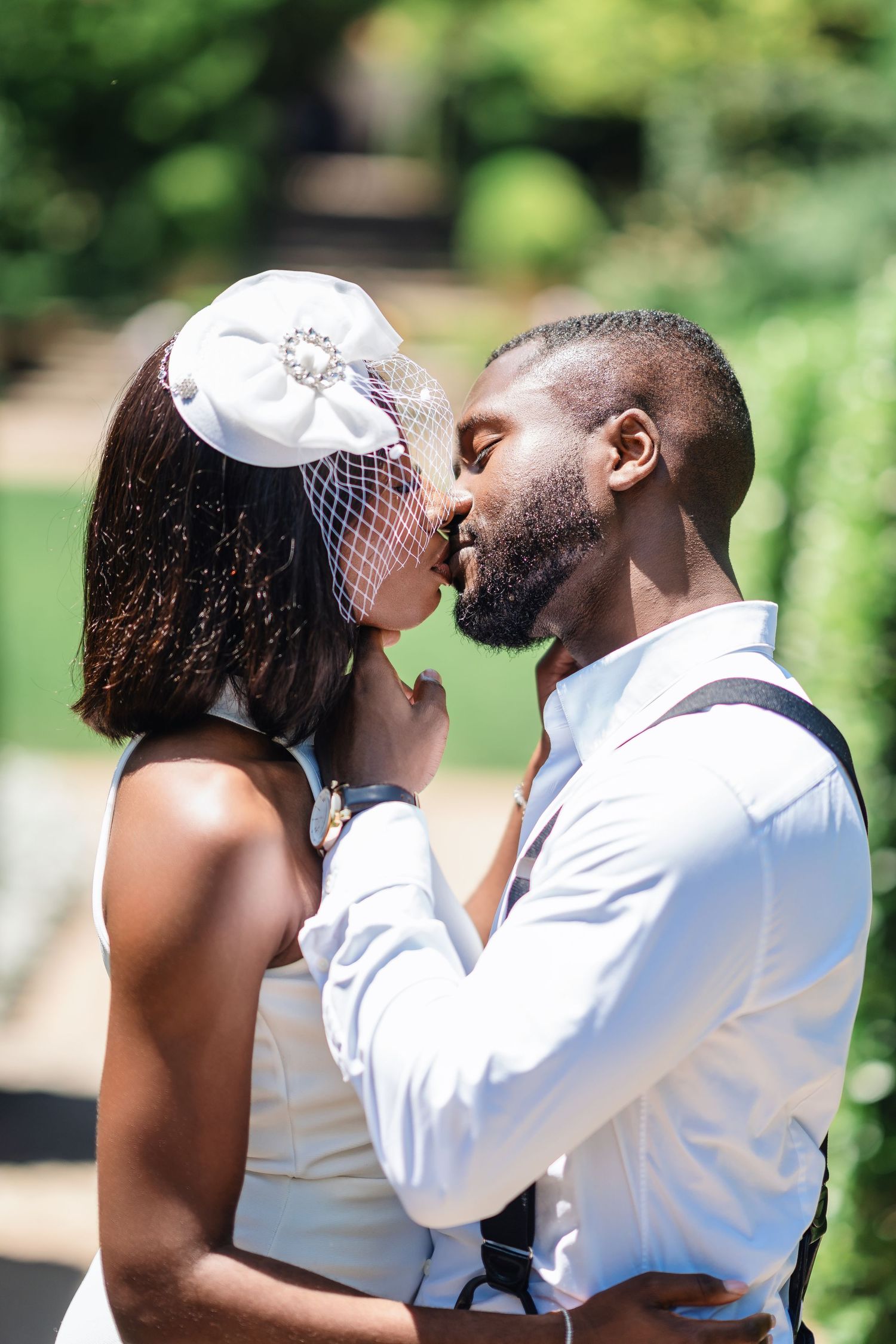 A tender moment between newlyweds in white and formal attire against a green garden backdrop.