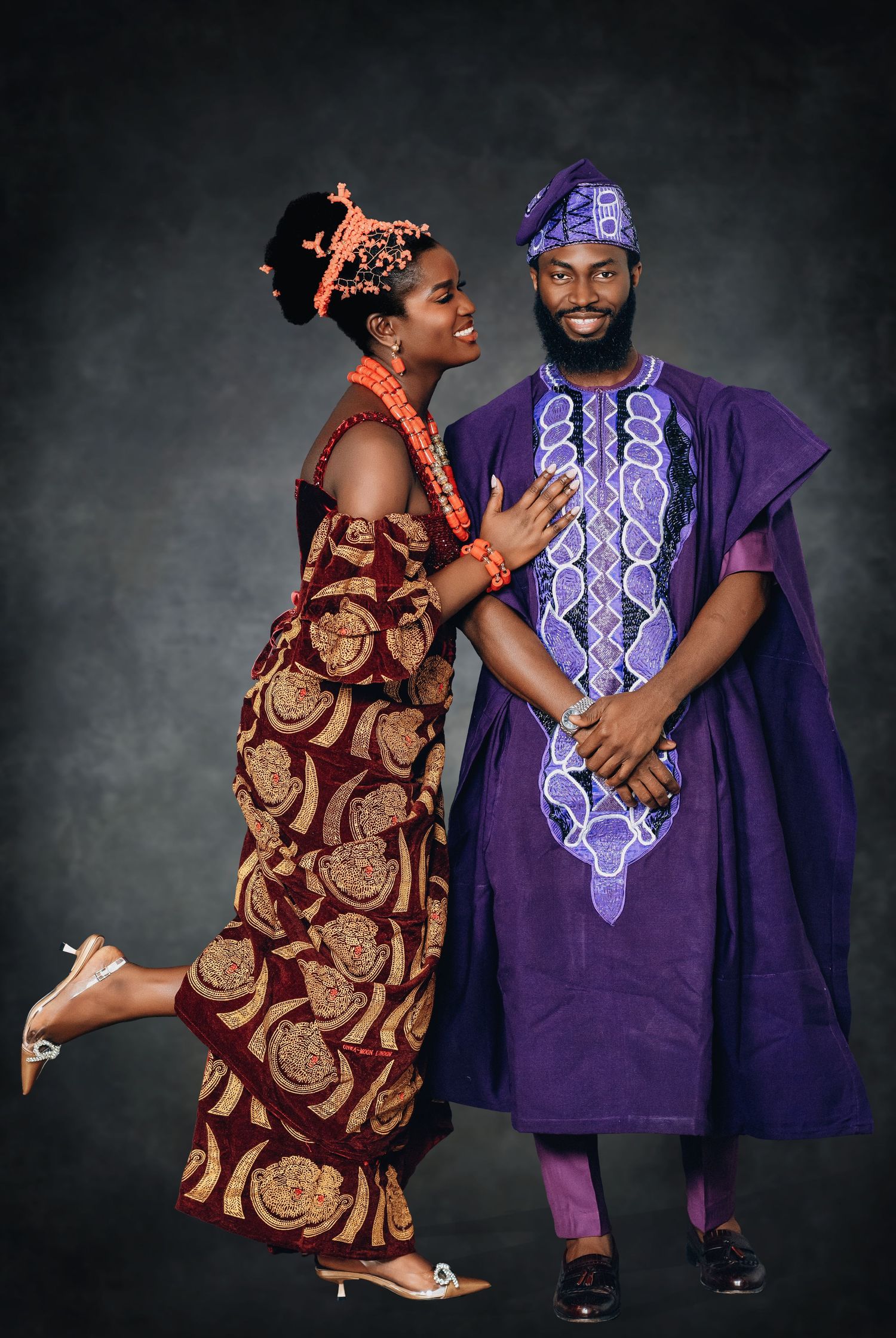 Couple in traditional Nigerian wedding attire with purple agbada and burgundy ankara dress posing playfully.