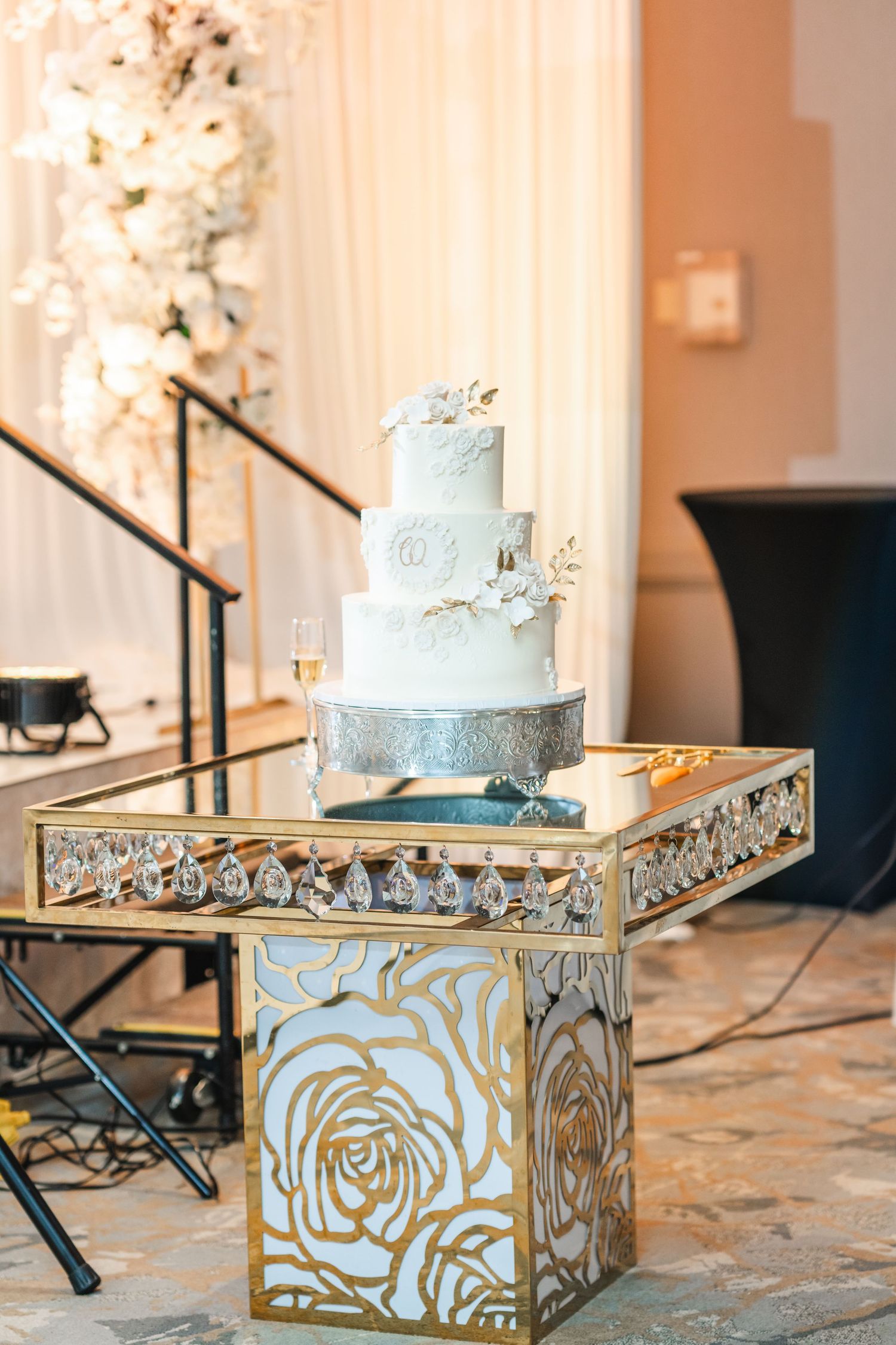 Pale blue wedding cake with delicate floral details displayed on an ornate gold mirrored stand.