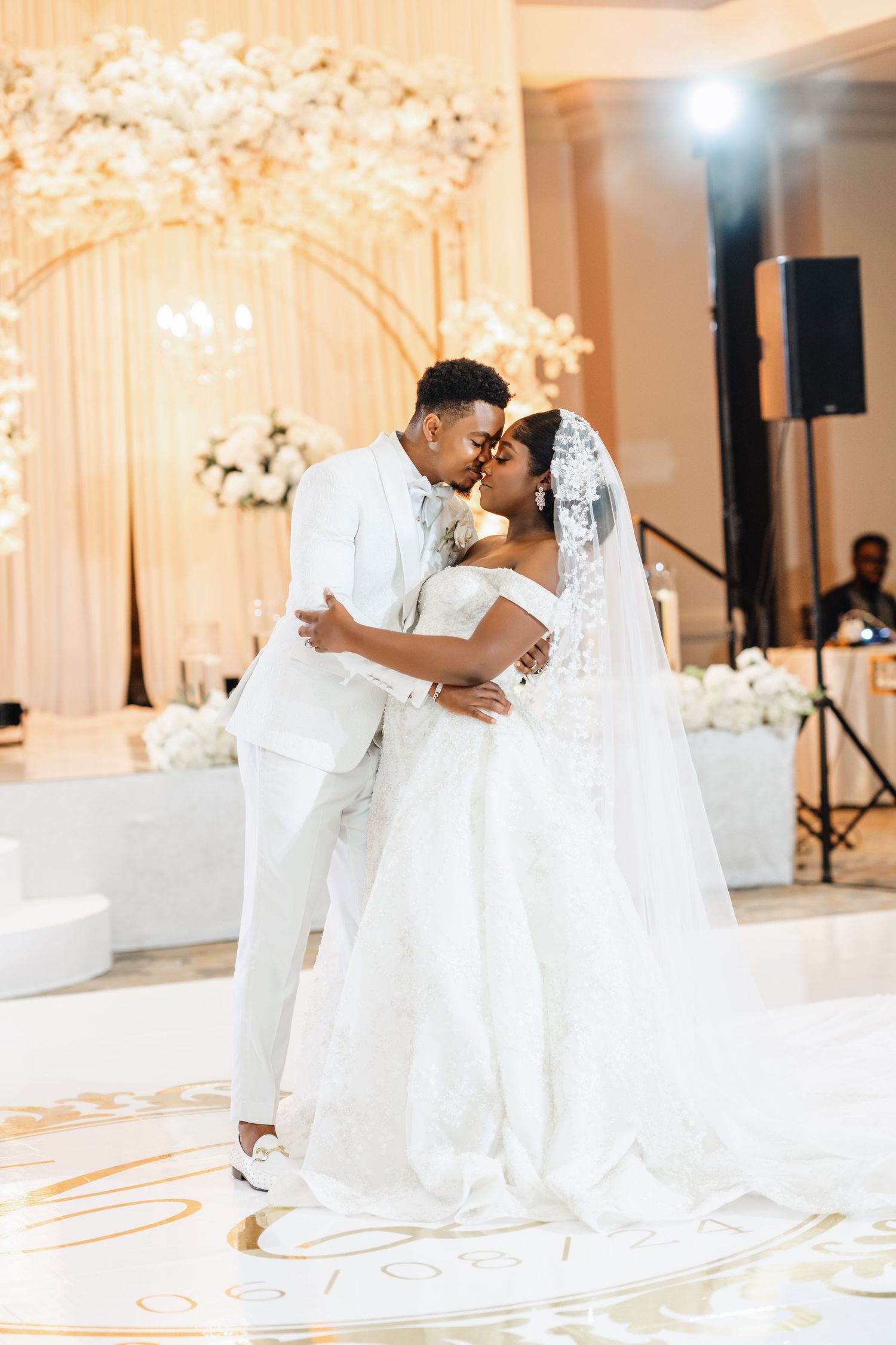 A couple shares their first dance under a floral arch at their elegant white wedding reception.