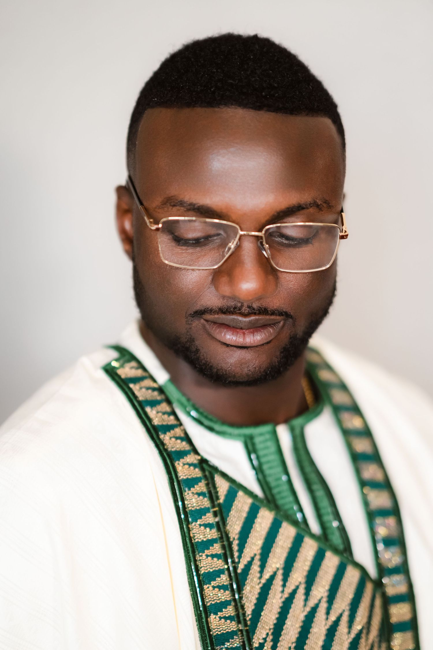 Close-up headshot of someone smiling while wearing glasses and traditional African attire.