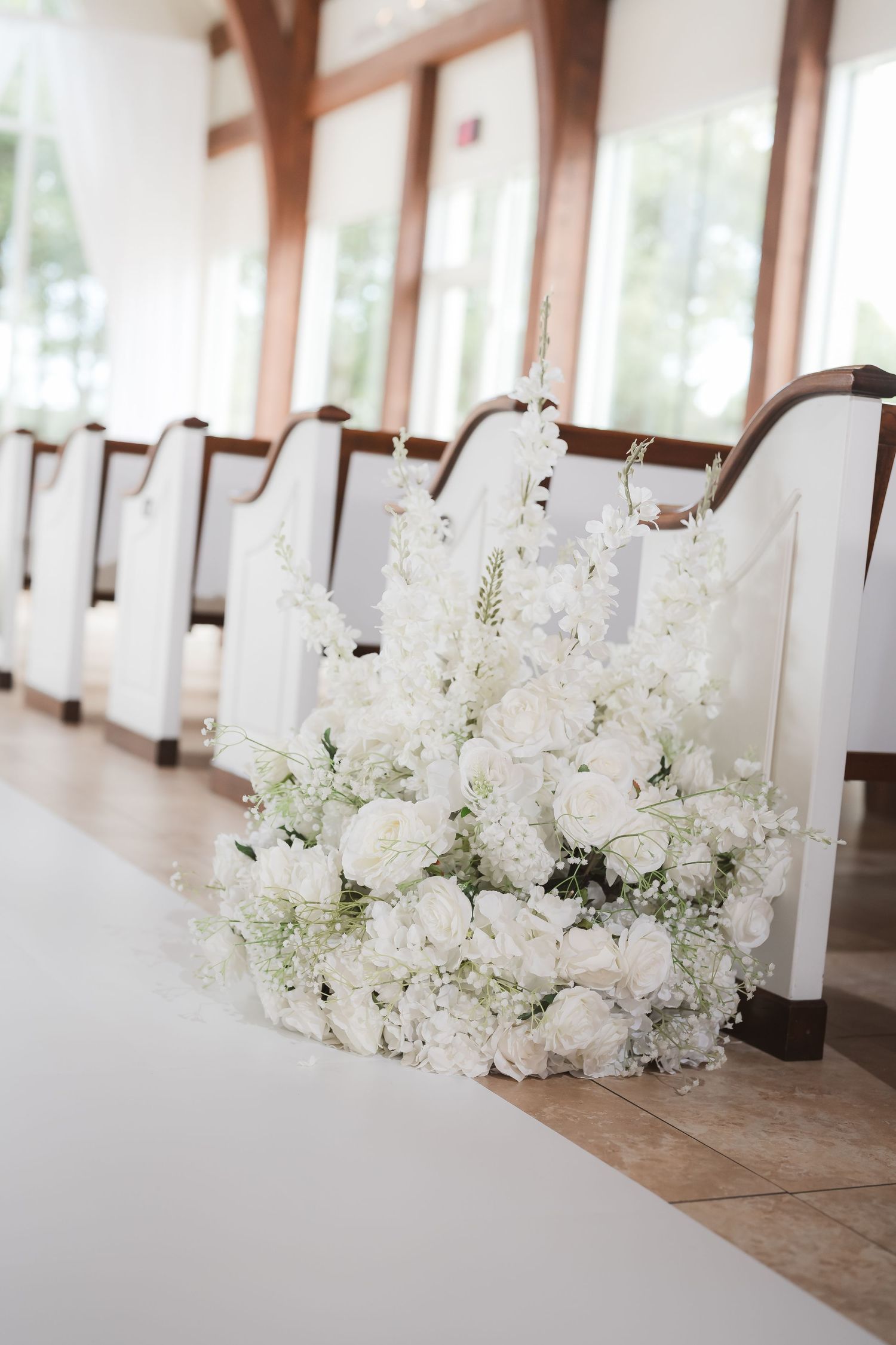 White floral arrangements with delicate blooms line a wedding ceremony space with wooden accents.