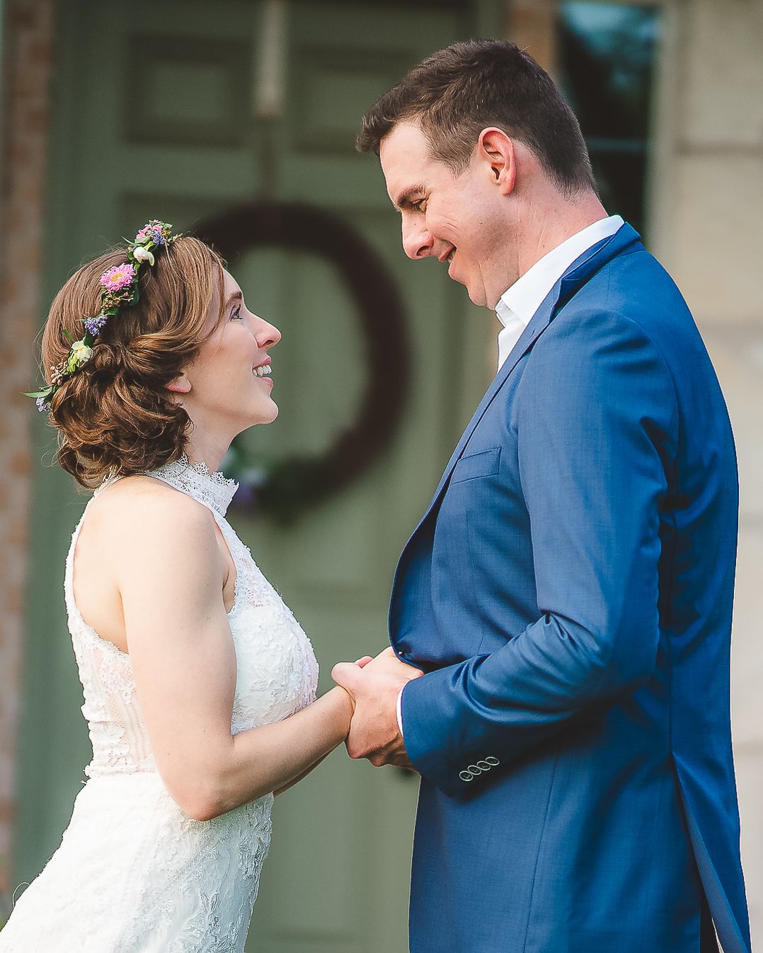 A bride in a white dress with floral crown and groom in navy suit share a joyful moment together outdoors.