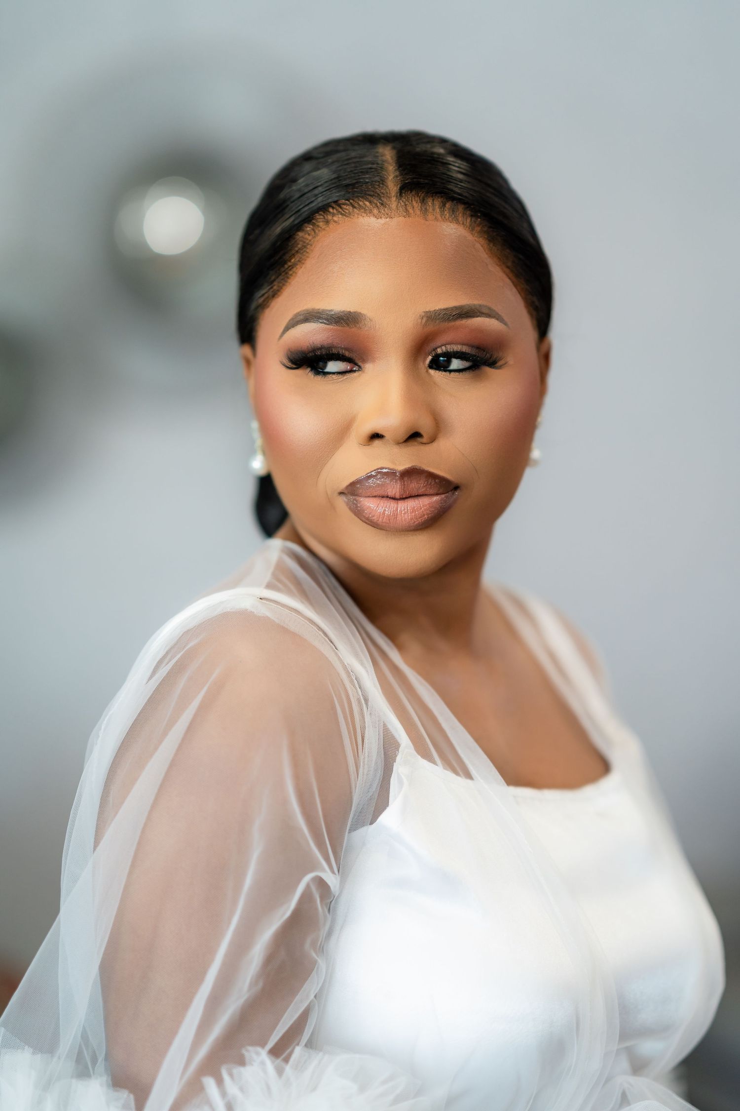 Elegant bridal portrait showcasing a sheer-sleeved white wedding dress with sleek styling.