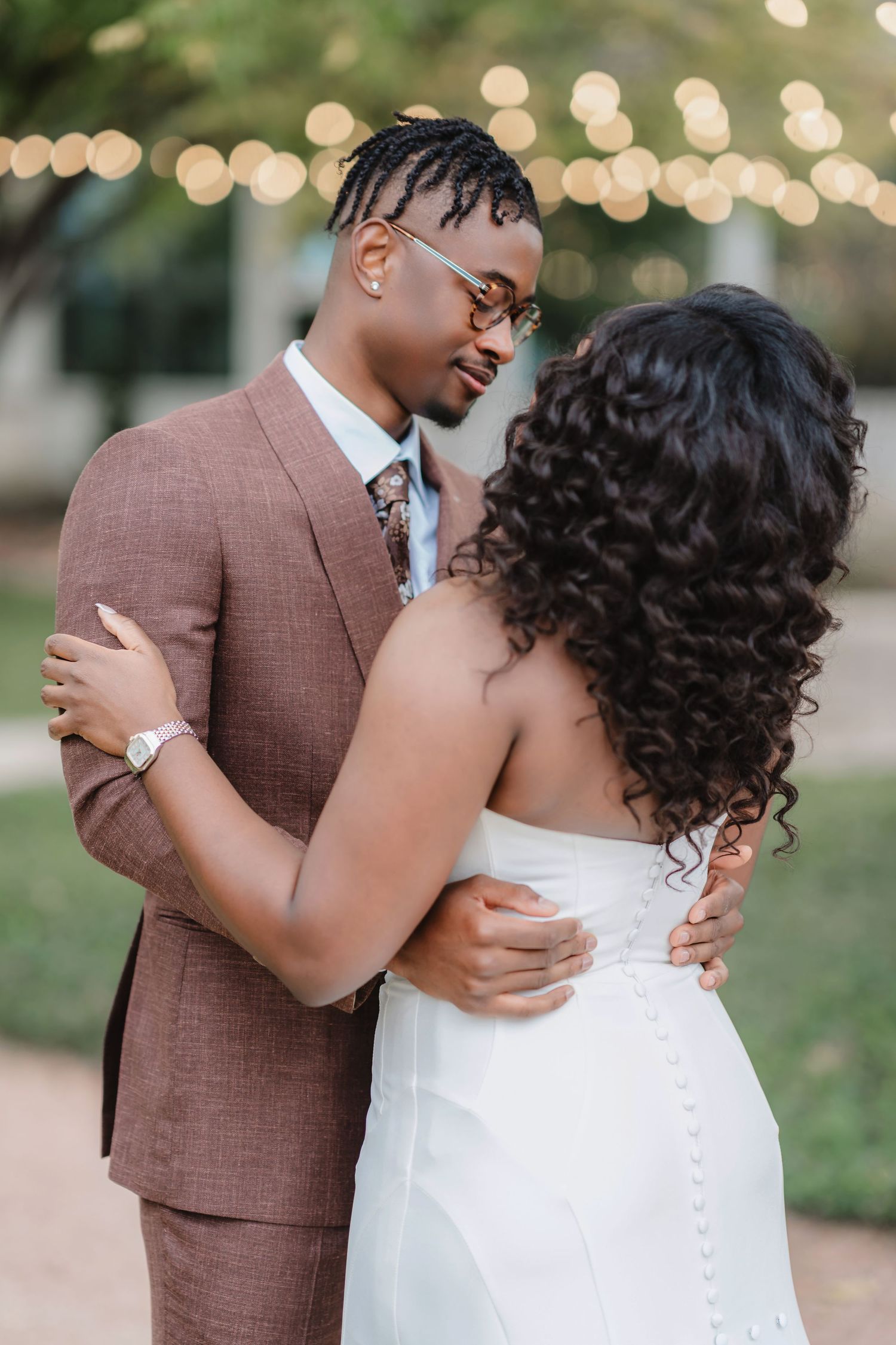 Romantic couple embraces during sunset wedding photos with twinkle lights in background.