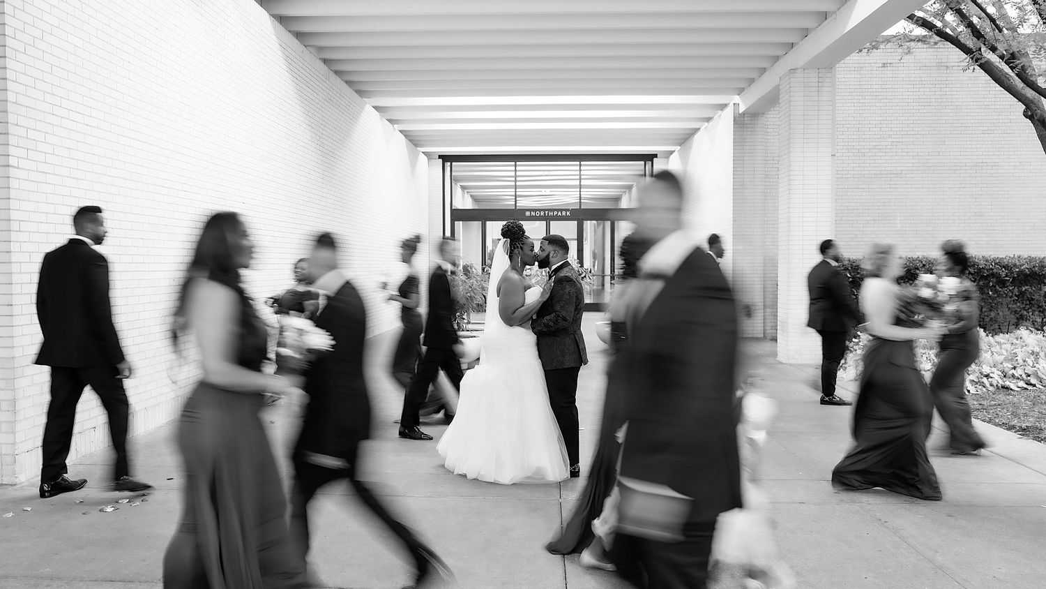 Time-lapse style photography of wedding guests in a modern white corridor.