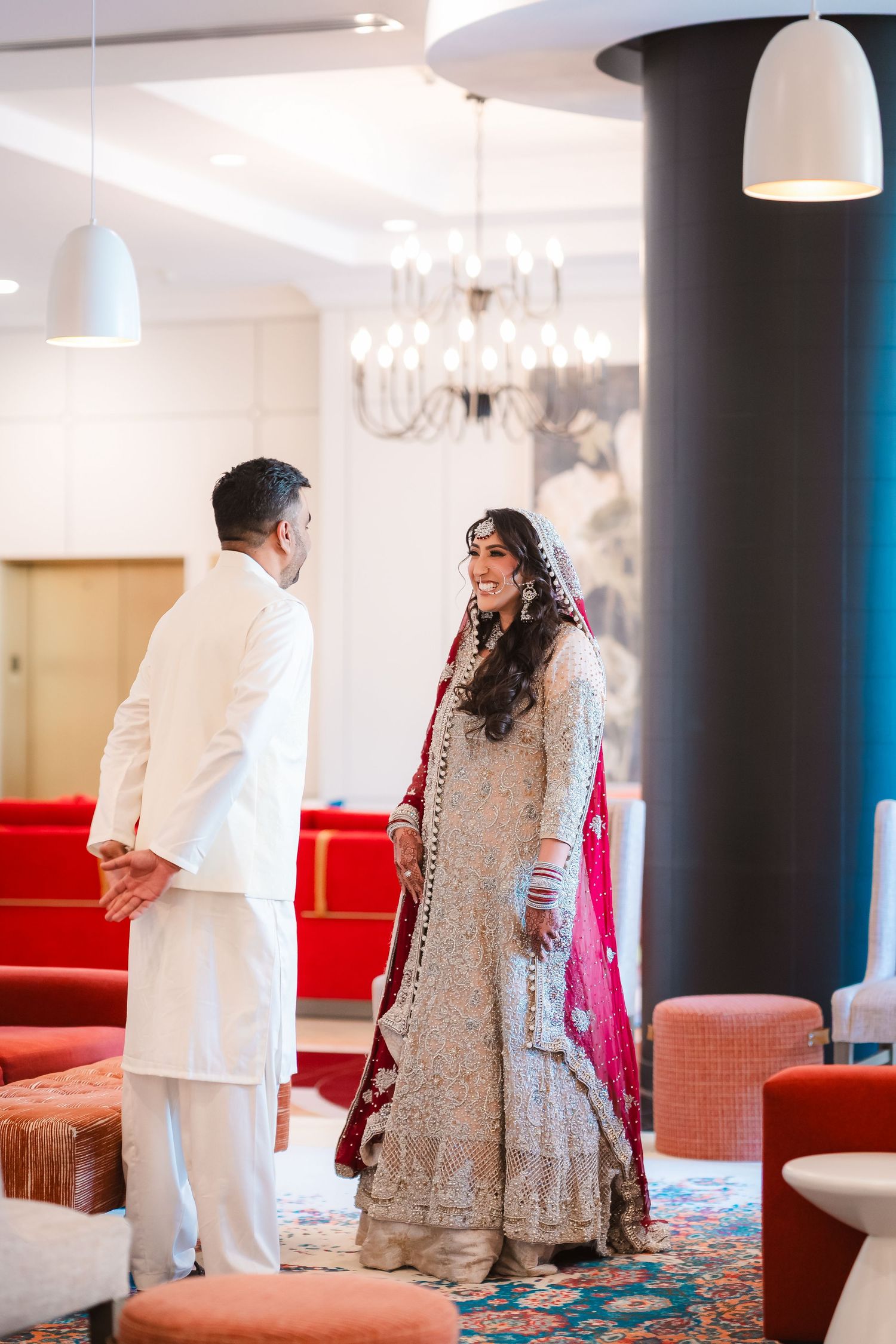 A traditional wedding first look moment captured in an elegant indoor venue with red seating.