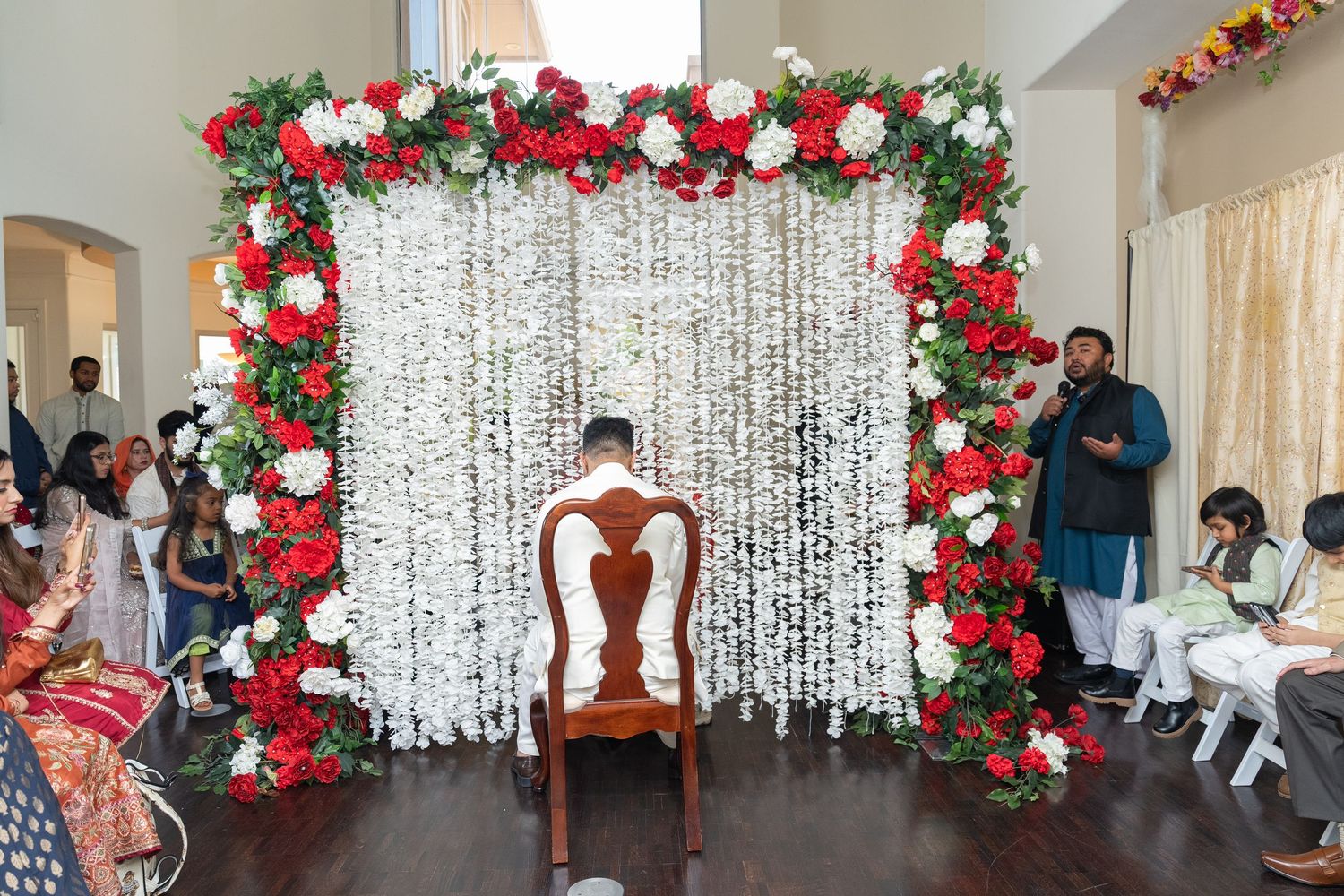 Wedding backdrop with white crystal curtains and red rose arch decorations.