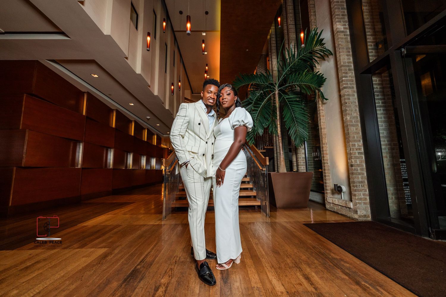 A couple in matching white outfits share an intimate moment on a wooden floor in an elegant indoor setting.