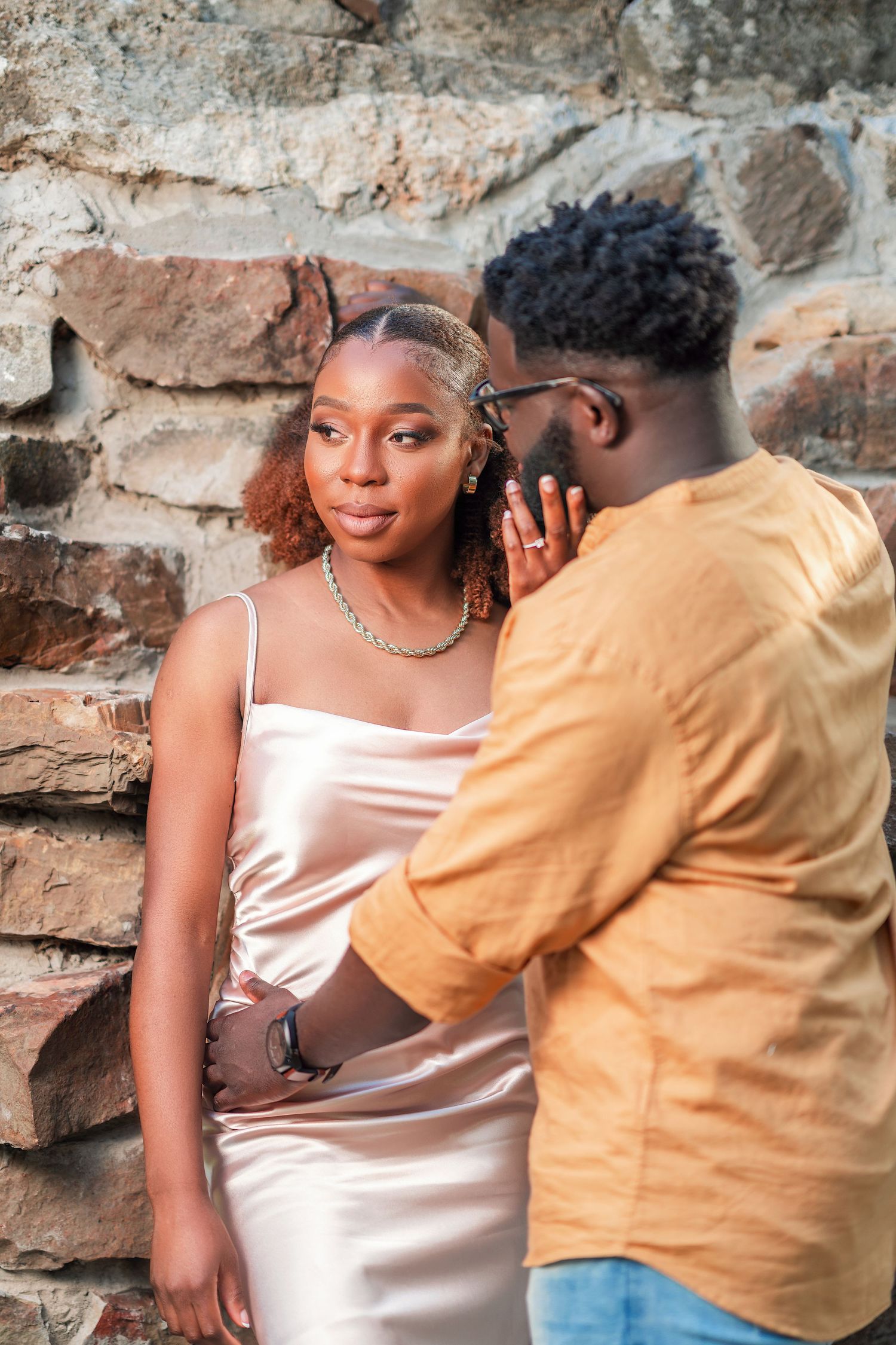 A couple shares an intimate moment against a rustic stone wall backdrop.